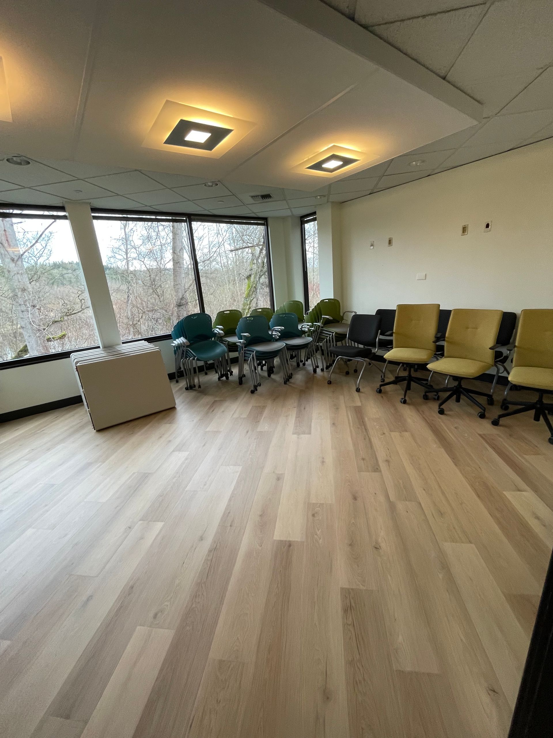 Empty conference room with wood flooring, chairs, and large windows with outdoor view.