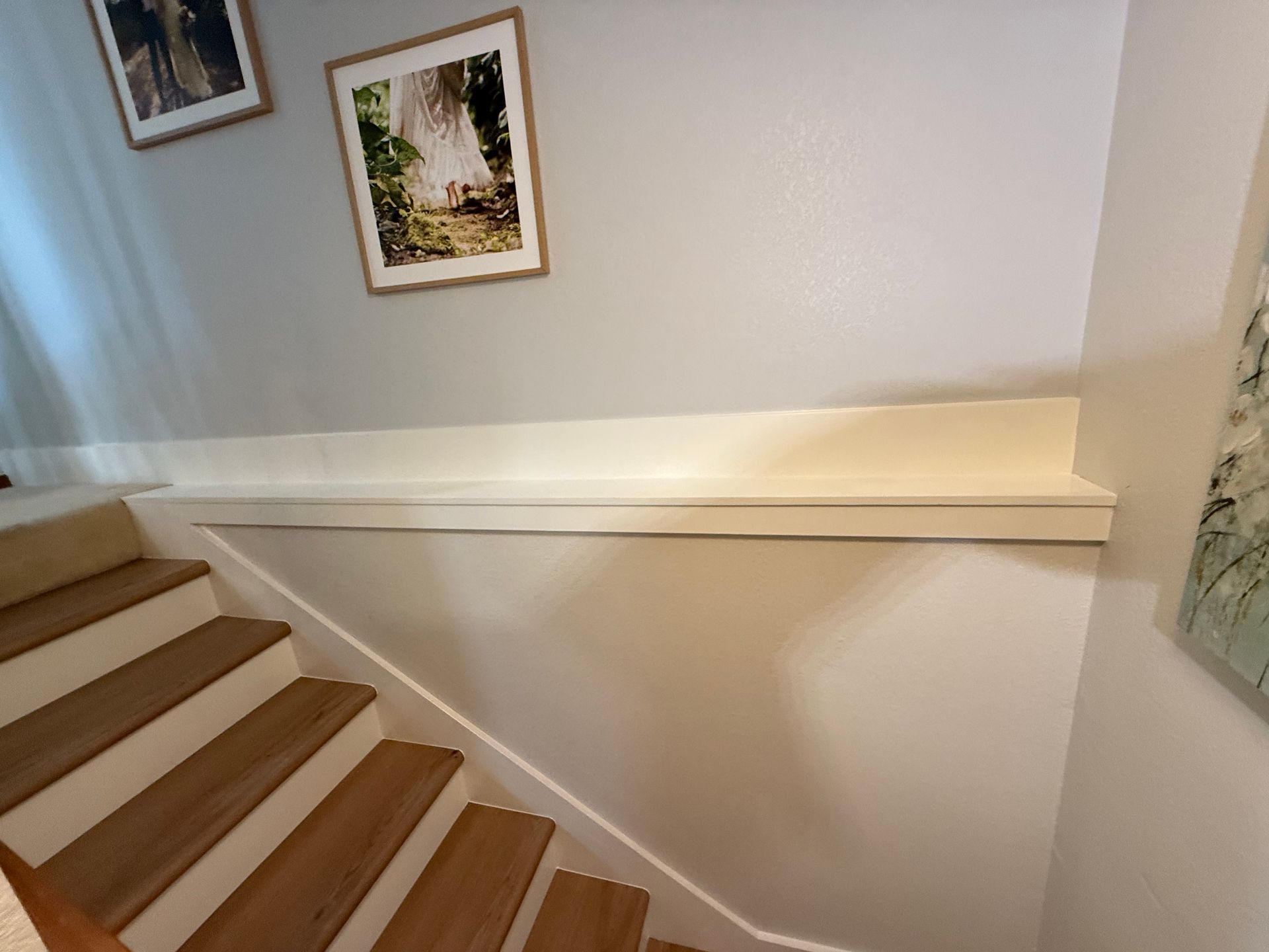 Staircase with wooden steps and a white shelf along the wall, two framed pictures above.