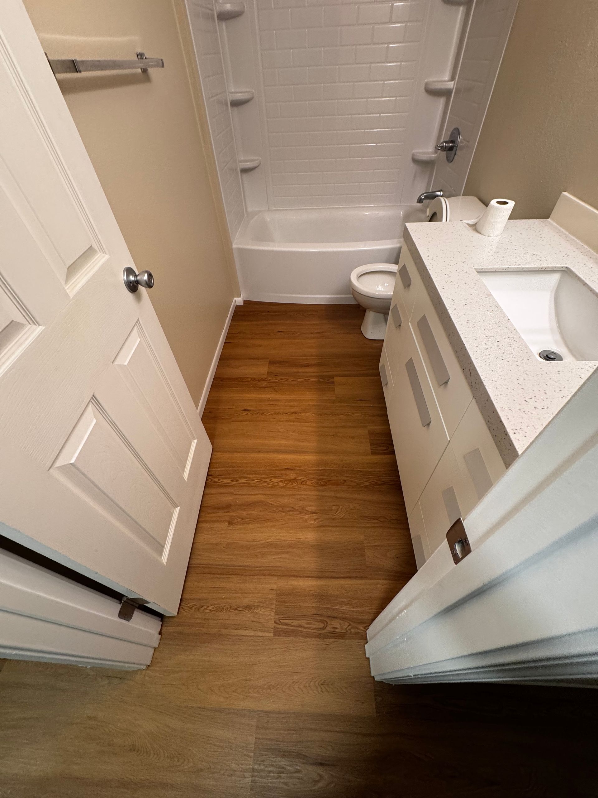 Bathroom with white sink, toilet, and bathtub. Wooden floor, white door, and tiled walls.