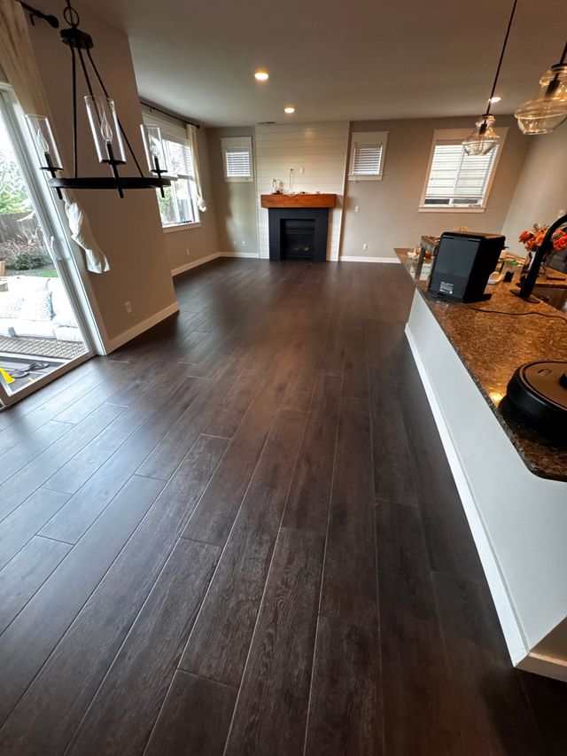 Dark wood floor in a living room with fireplace and large windows. Black chandelier hangs above.