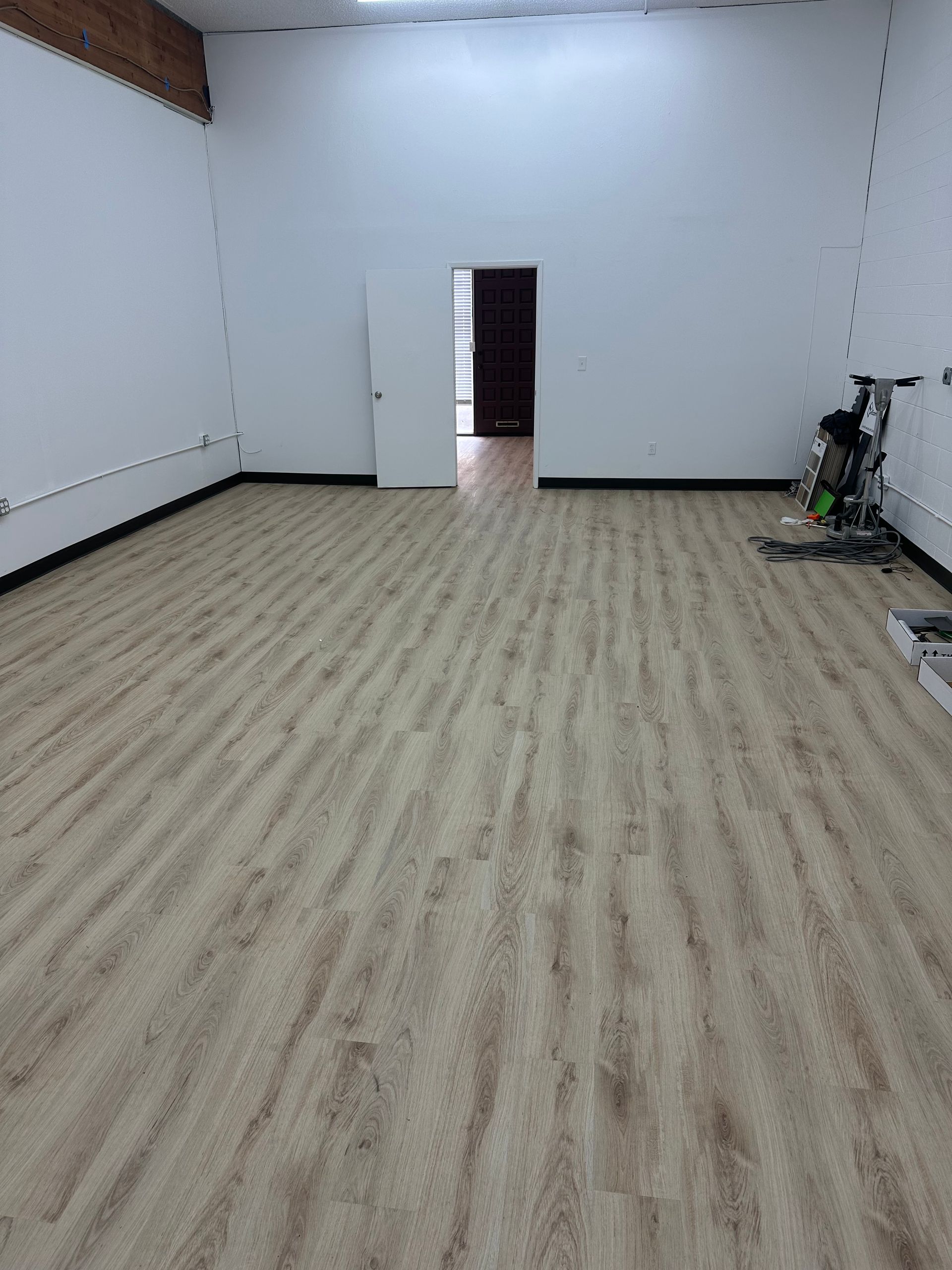 Empty room with light wood-look flooring, white walls, and a dark doorway in the distance.