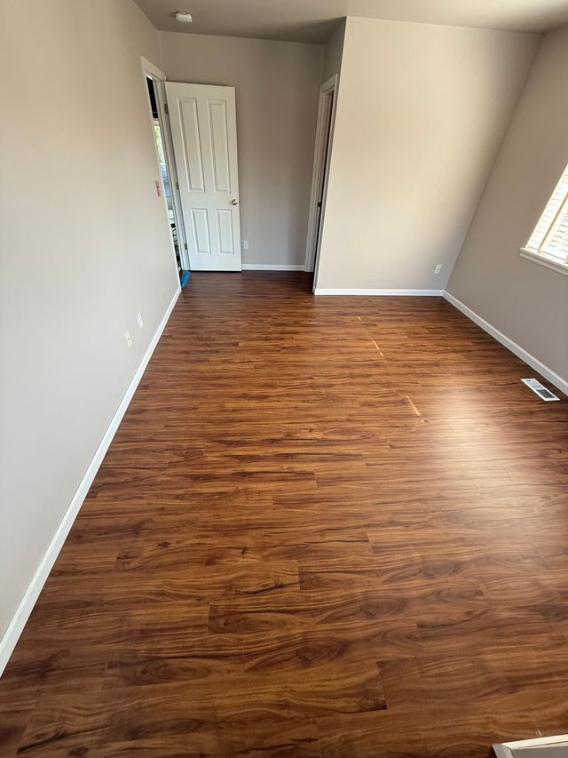Empty room with brown wood-look flooring, beige walls, and white door.