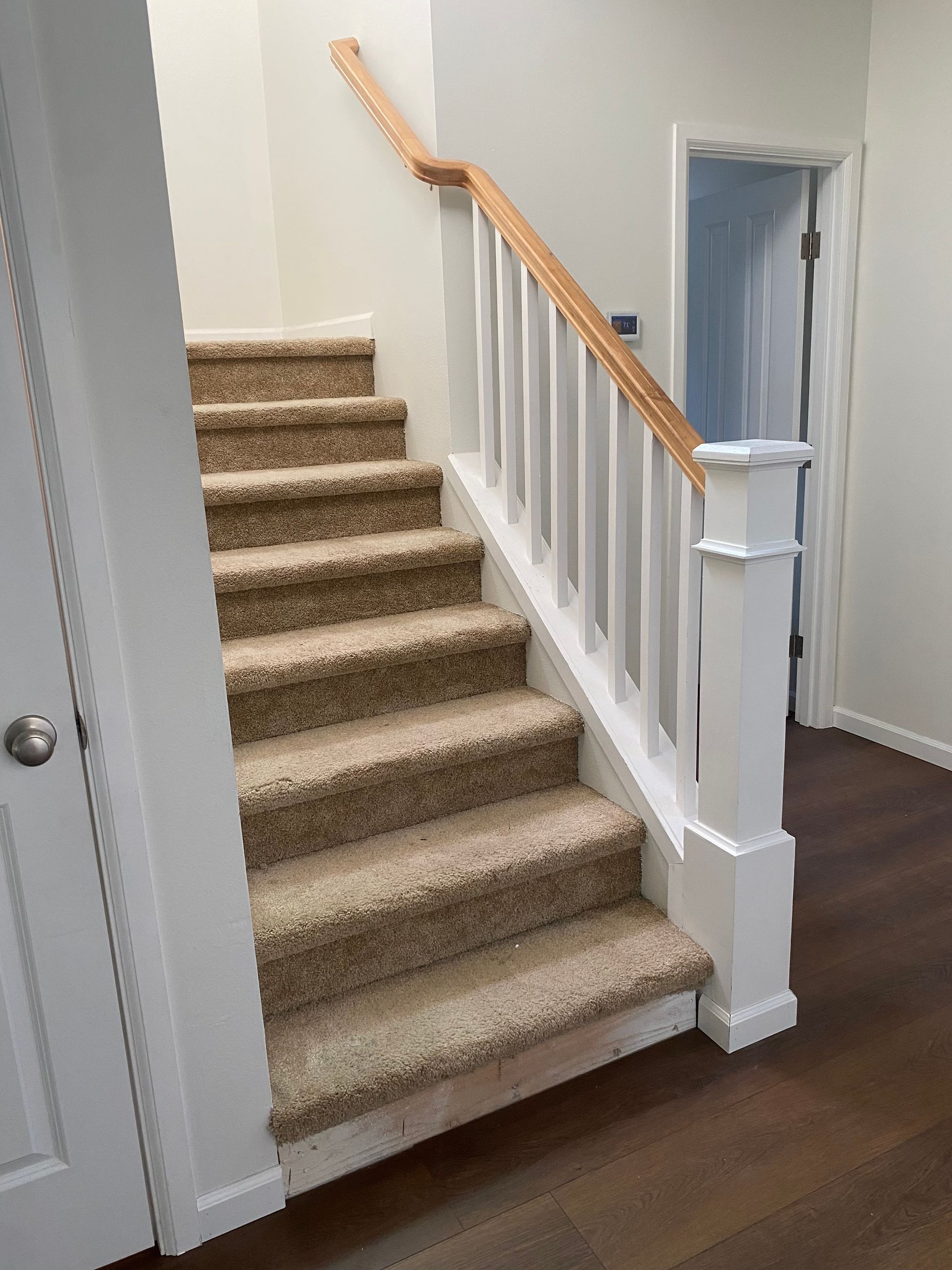 Staircase with carpeted steps and a wooden handrail, leading up. White painted spindles and trim.