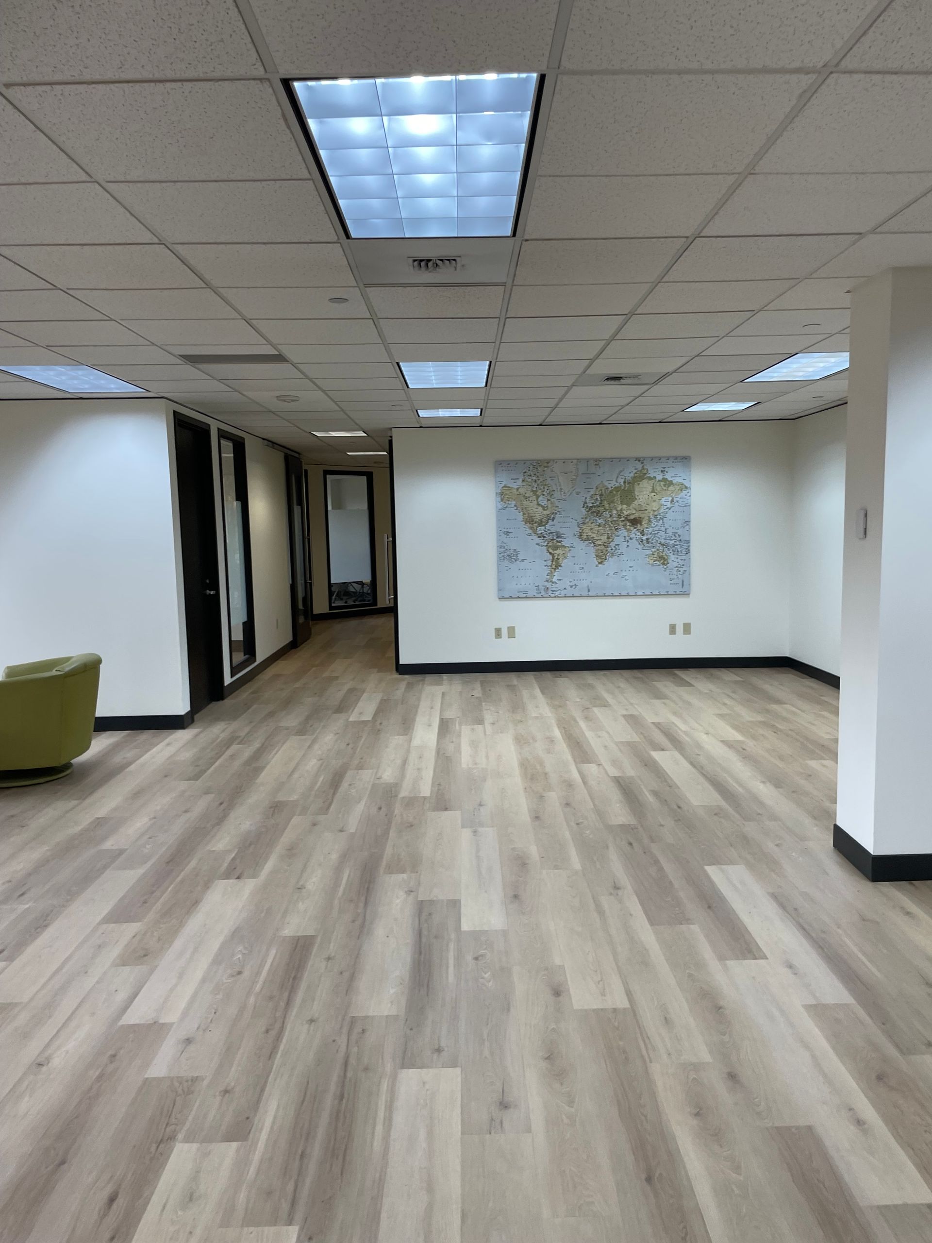 Empty office with light wood floors, white walls, map, and fluorescent ceiling lights.