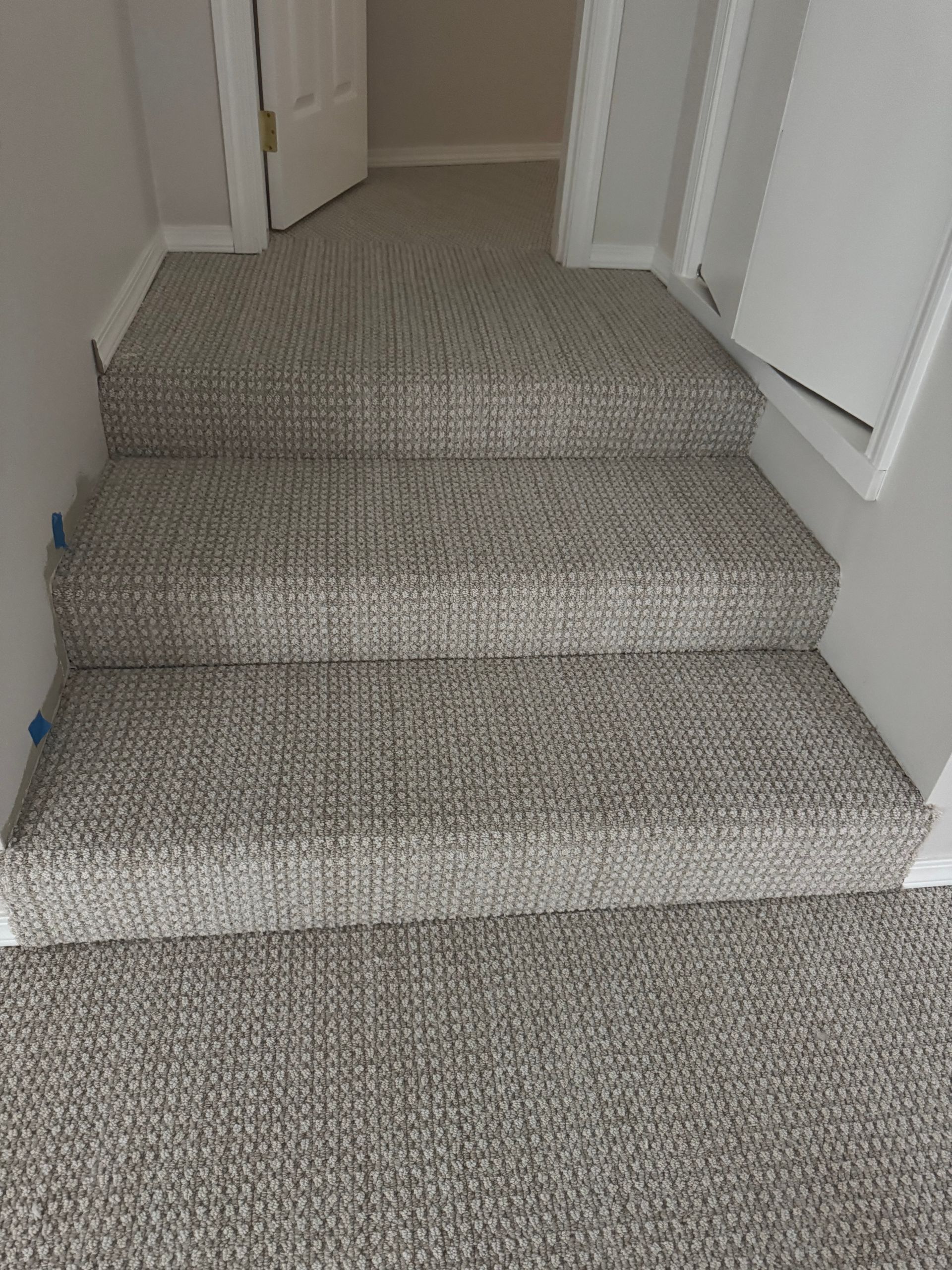 Carpeted staircase in a home; gray and white flecked carpet covers stairs and hallway, white trim.