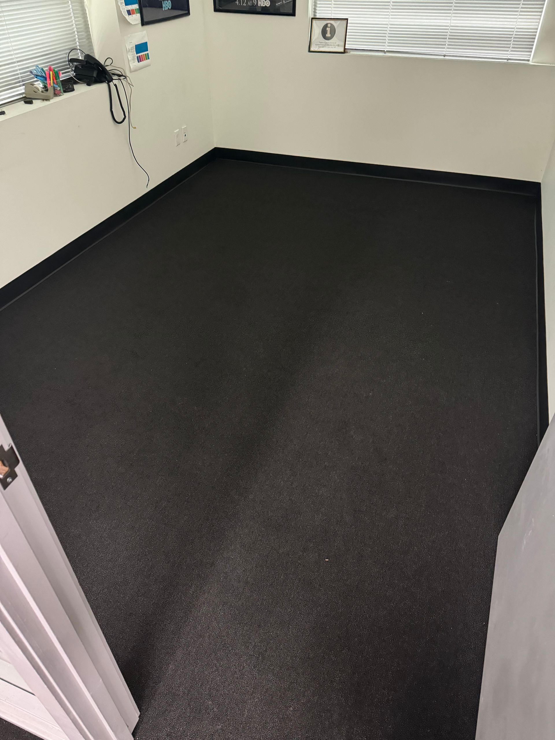 Small office room with black speckled flooring, white walls, and a window with blinds.