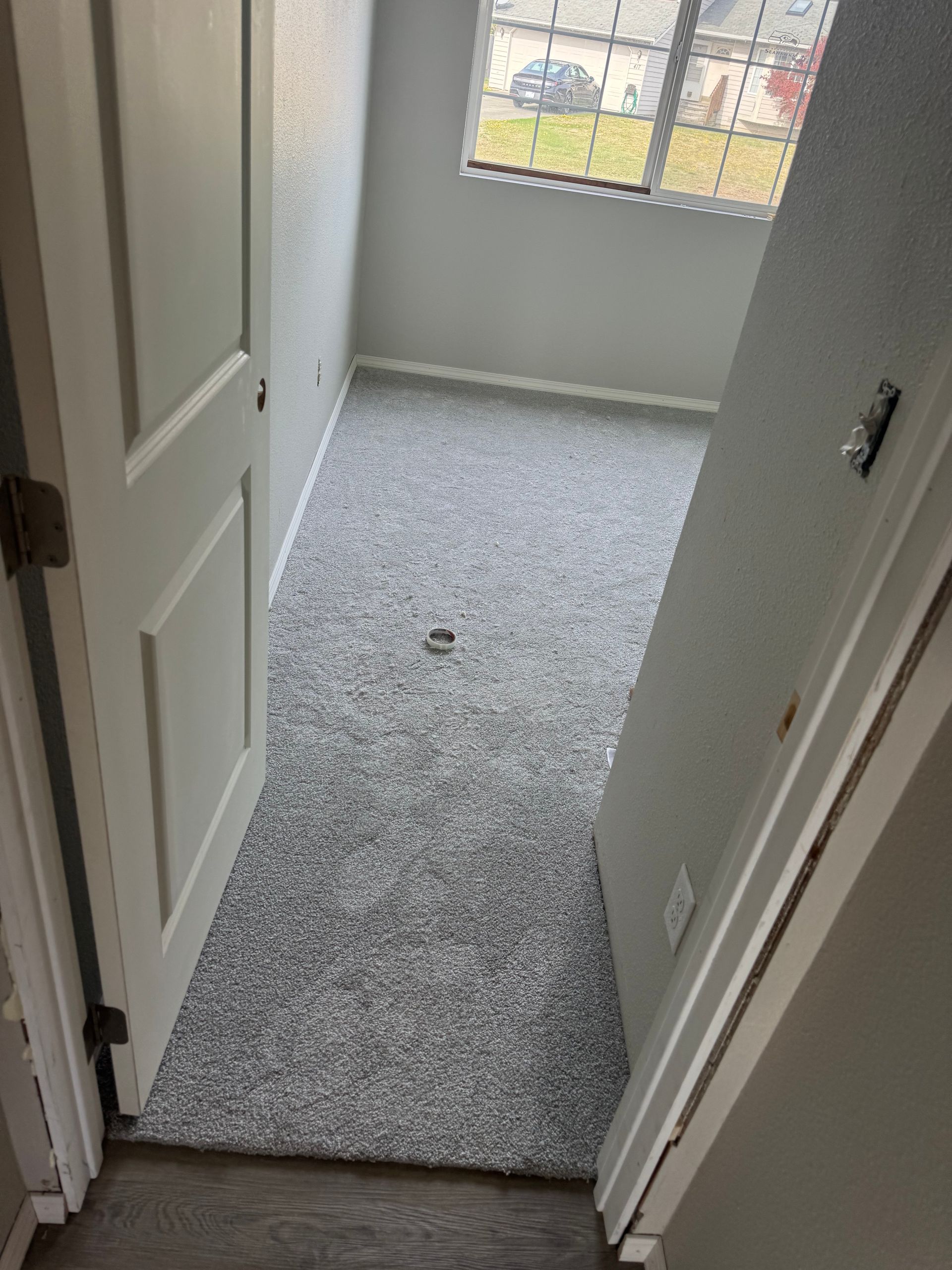A doorway leading into a room with gray speckled carpet and a window.