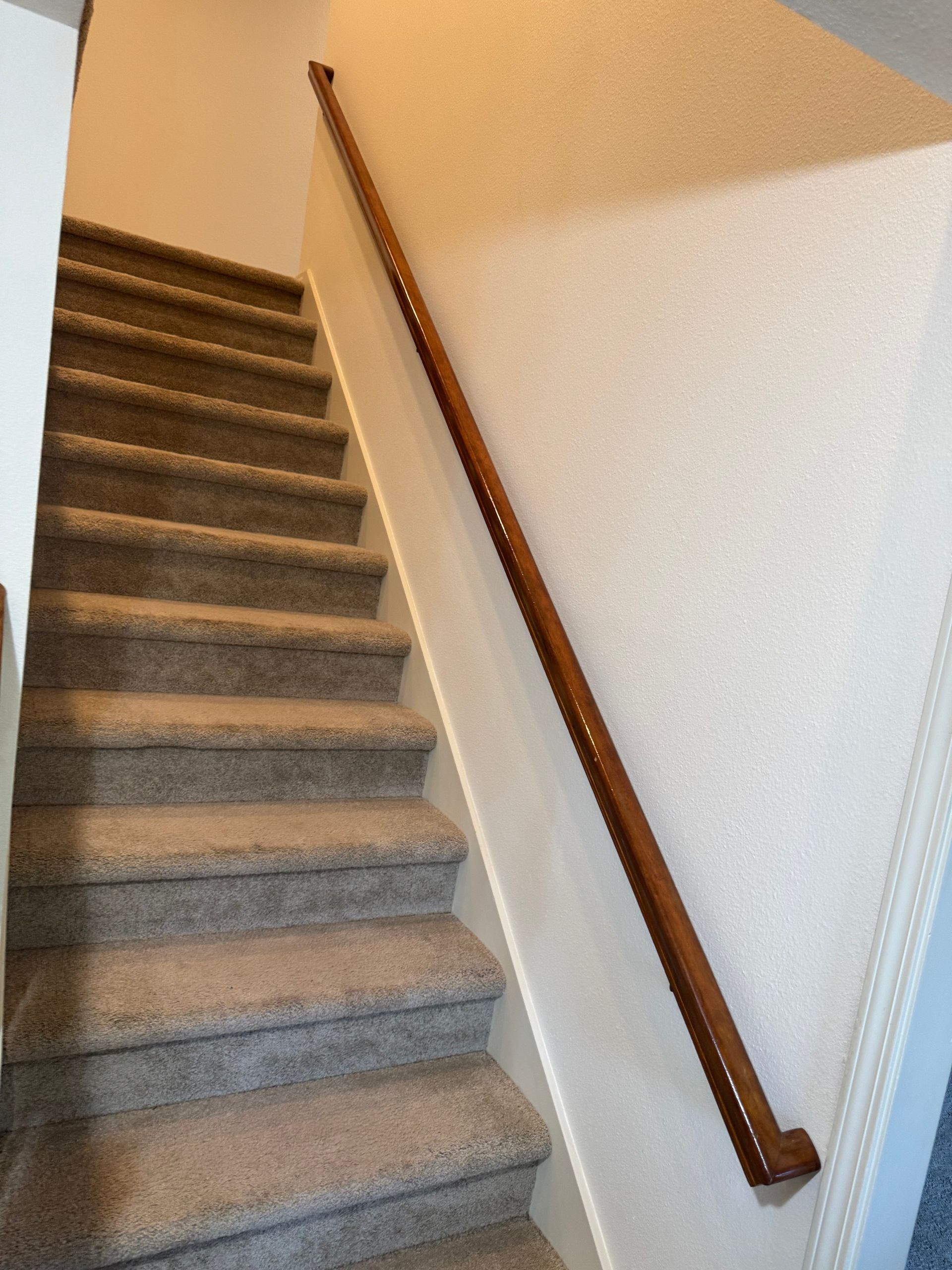 Staircase with carpeted steps and a wooden handrail on a white wall.