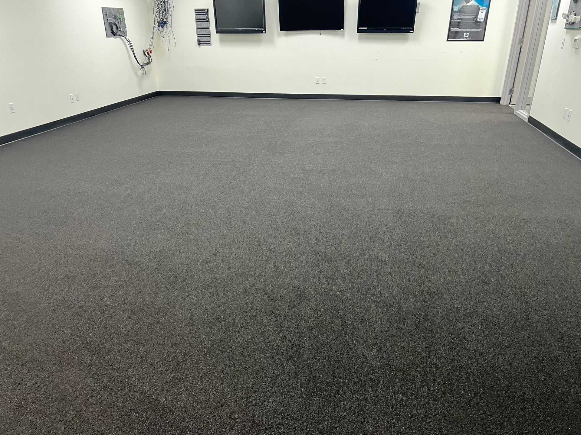 Empty room with dark gray carpet, white walls, and monitors.