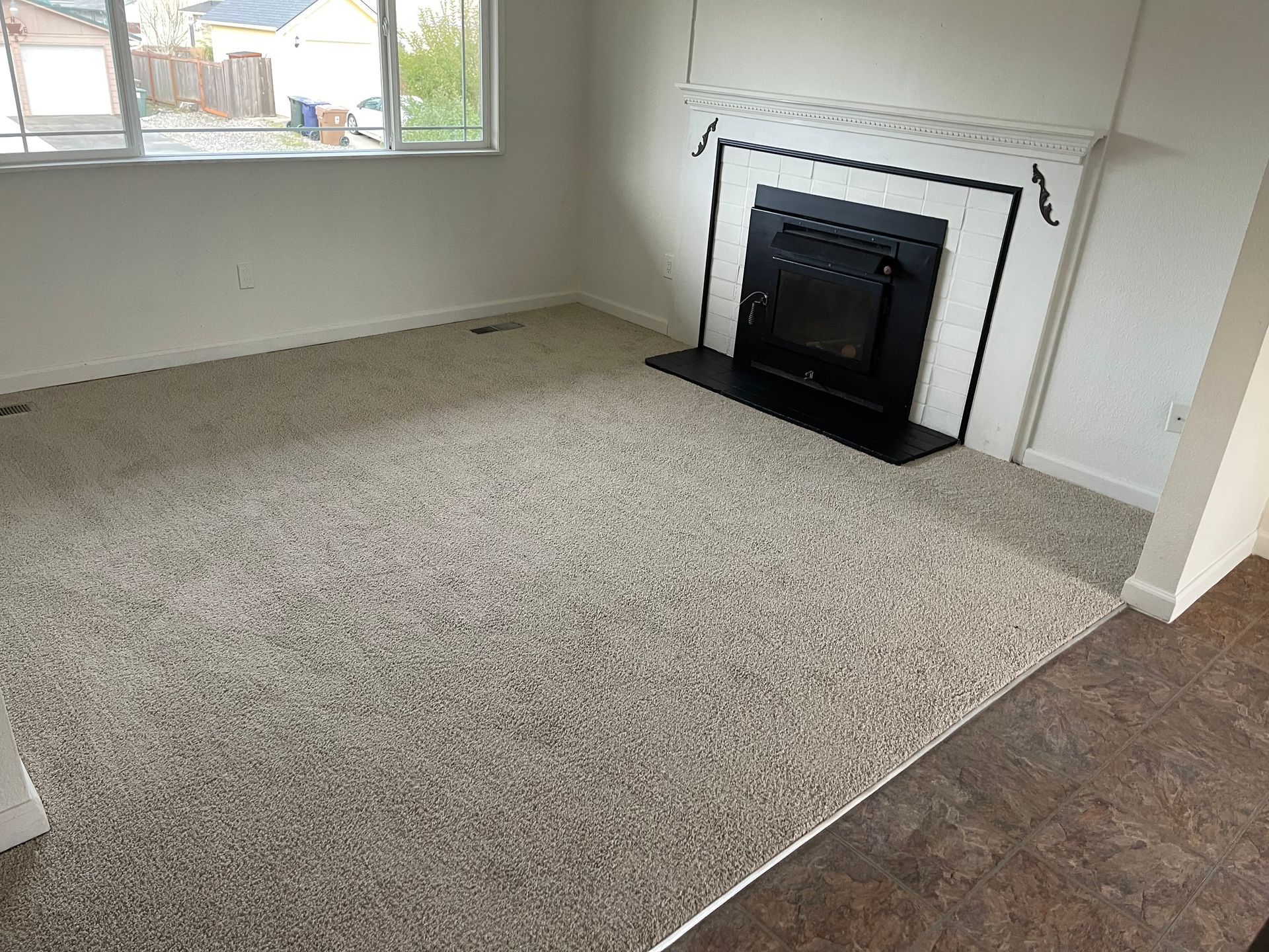 Empty living room with beige carpet, fireplace, and window.