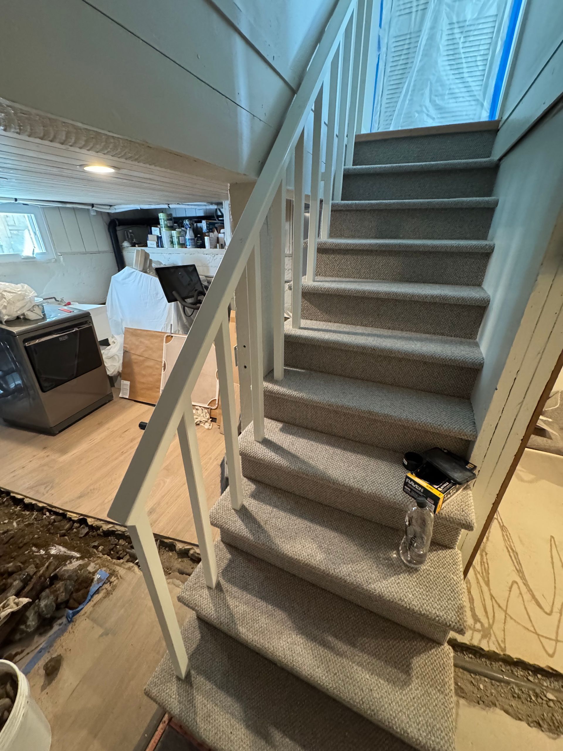 Carpeted staircase with white railing leading to a partially finished basement.
