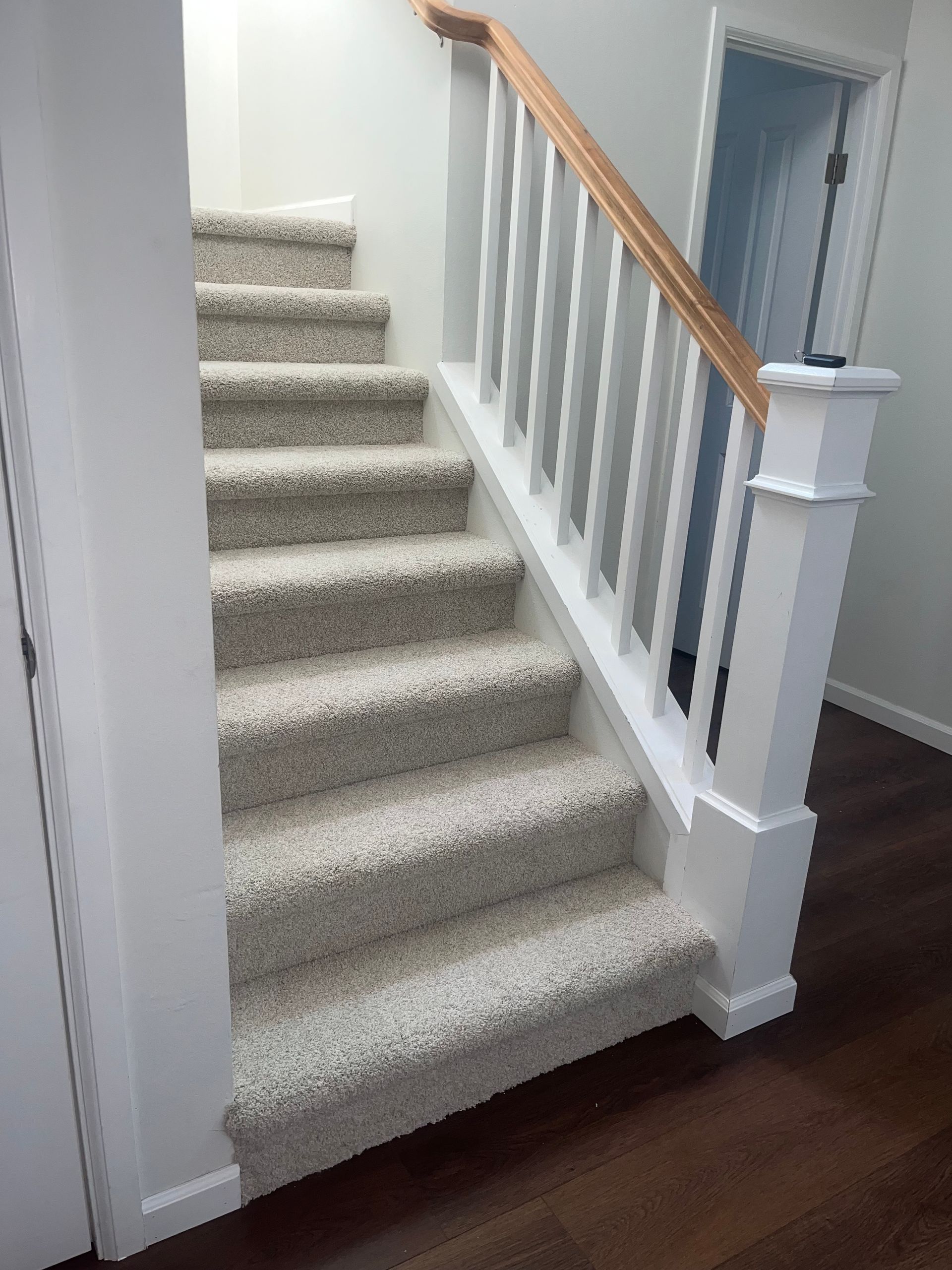 Carpeted staircase with white balusters, wooden handrail, and dark wood flooring.