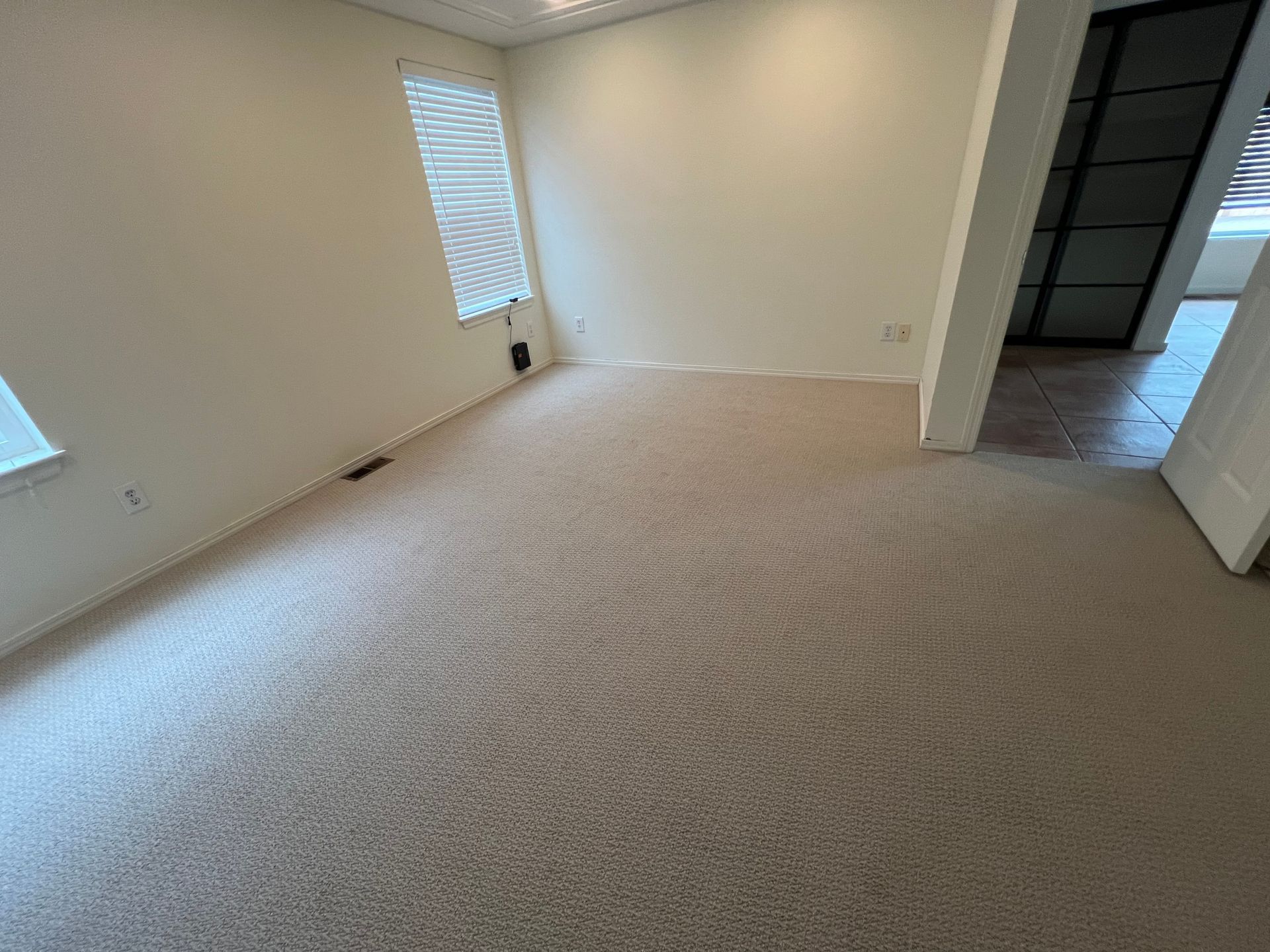 Empty room with beige carpet and walls, a window with blinds, and a doorway.