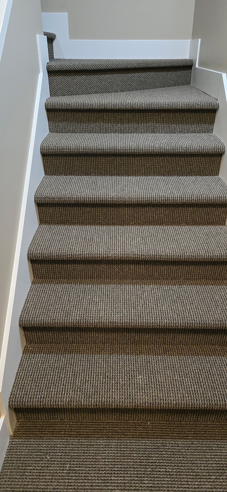 Staircase with patterned brown and gray carpet. White walls on either side.