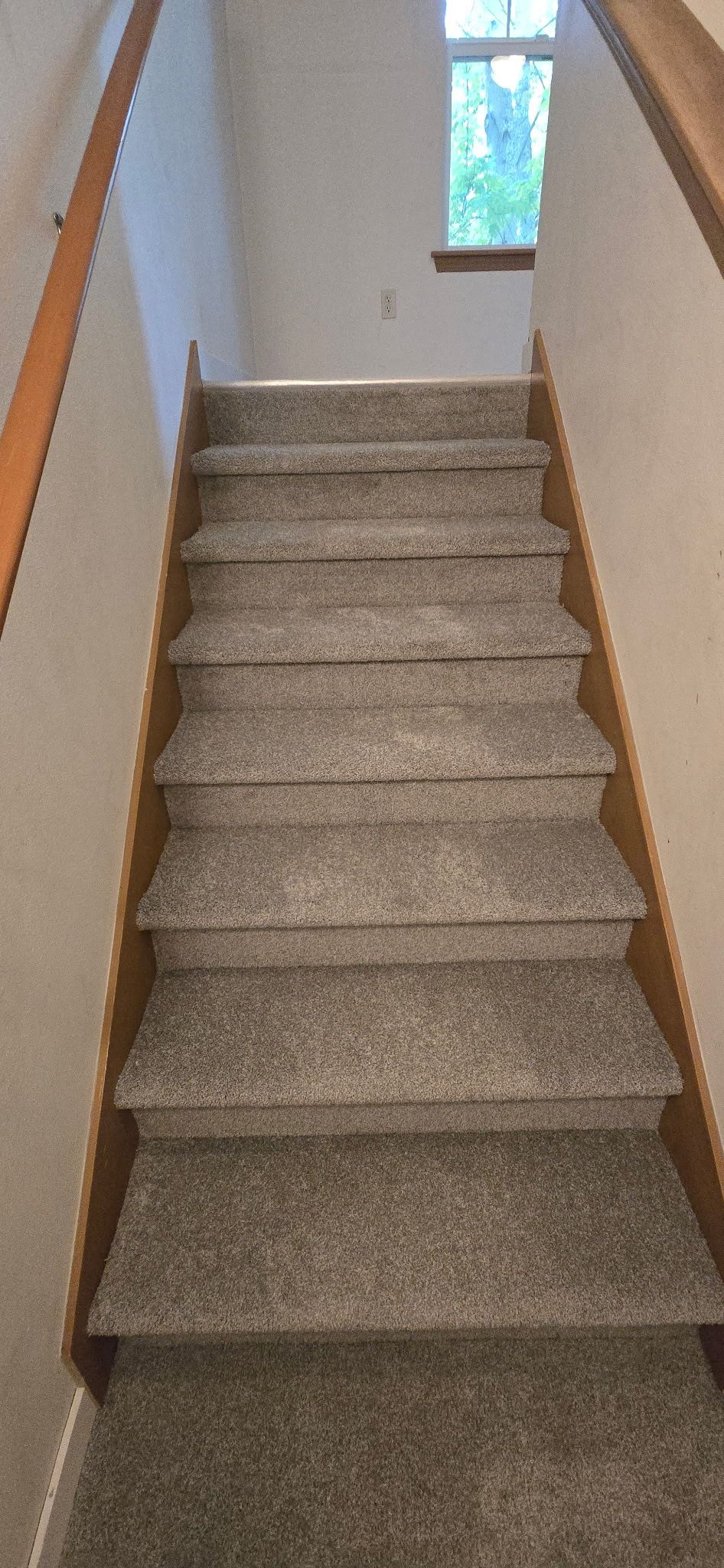 Staircase with gray carpet steps, wooden trim, and handrail. A window is at the top.