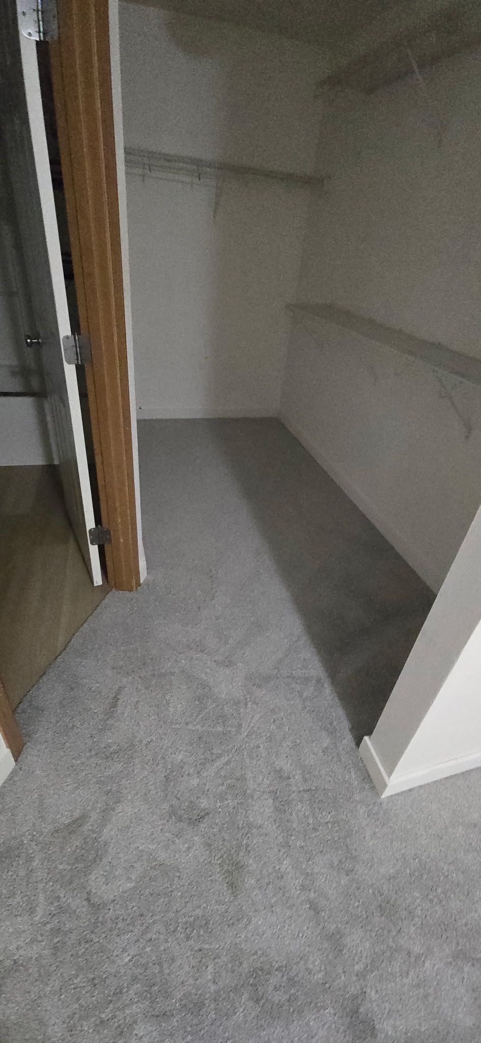 A narrow walk-in closet with gray carpet, white walls, and wire shelving.