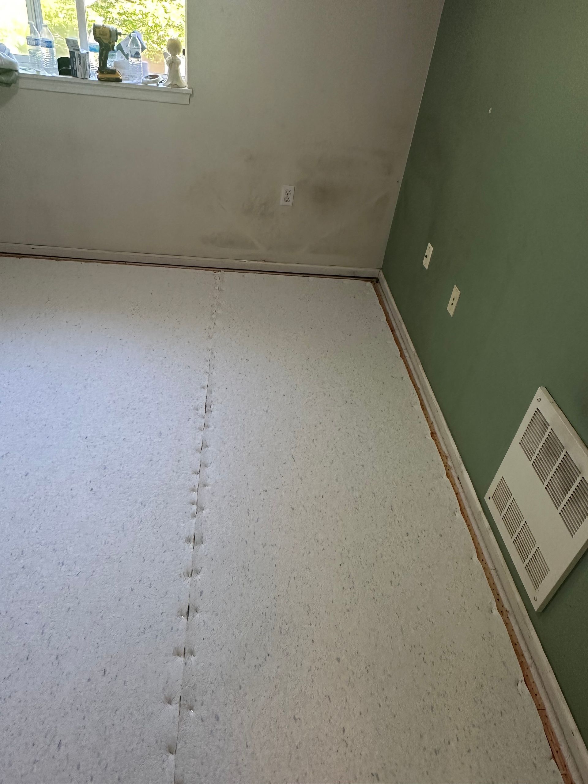 Room with white underlayment, green wall, and an open window.