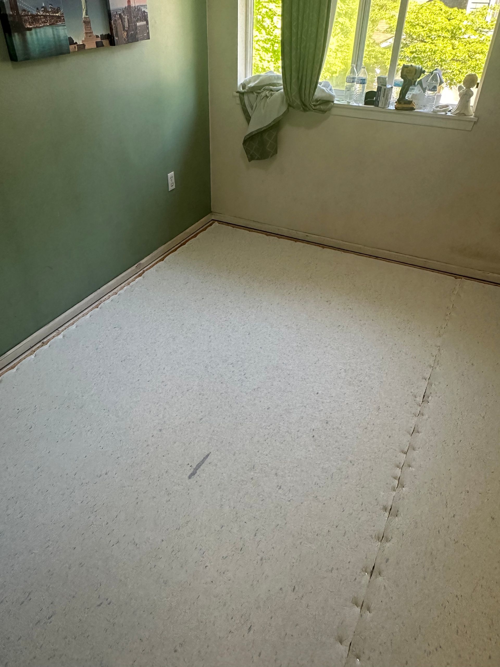 Room with speckled flooring, green wall, window with curtain, and baseboard.