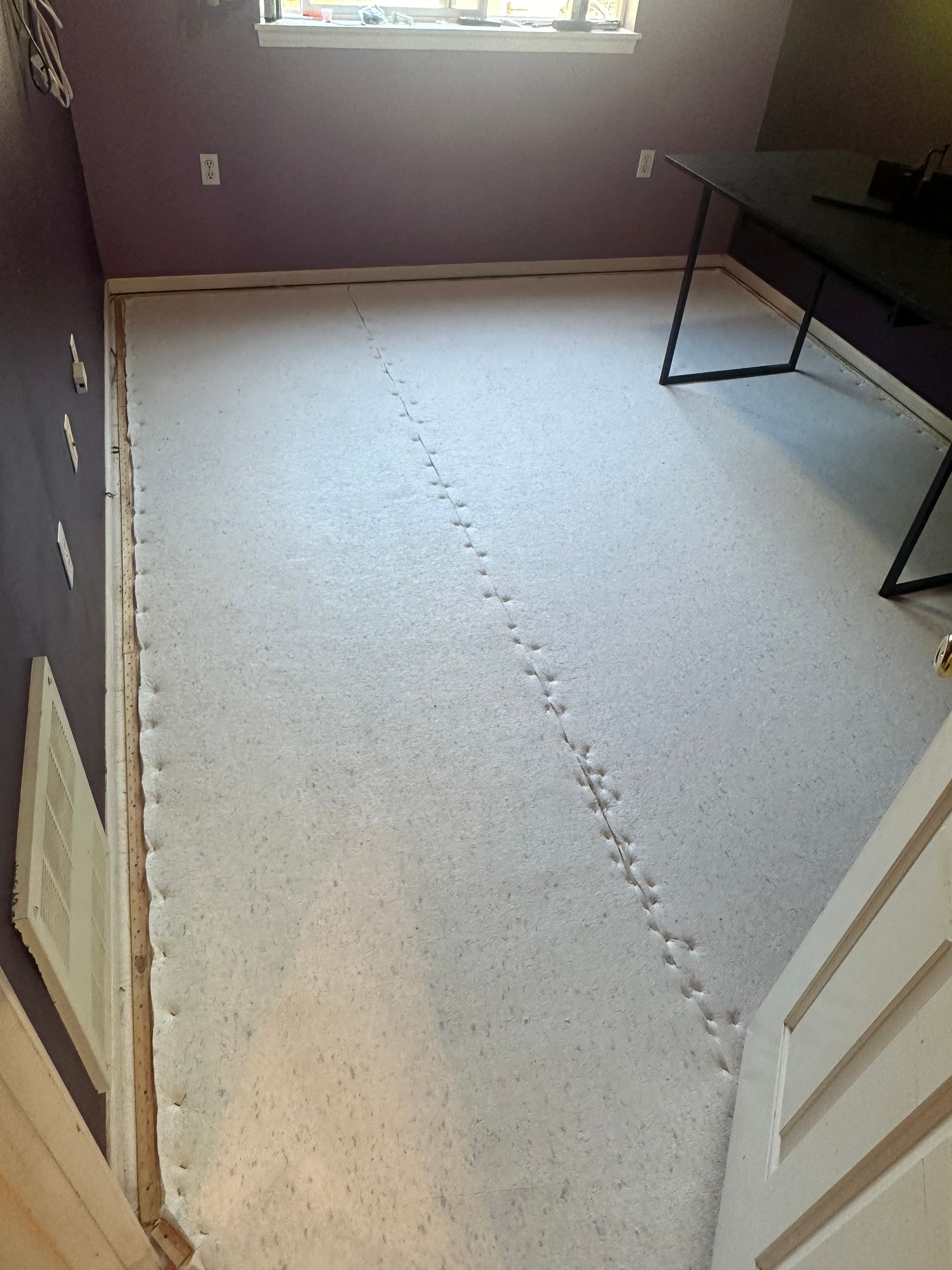 Footprints trail across a white-carpeted room with purple walls, a window, and a desk.