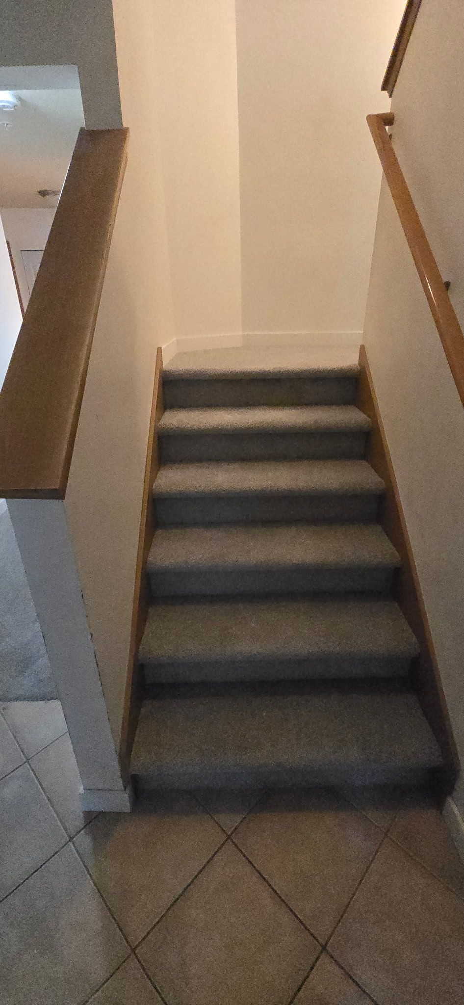 A staircase with gray carpet leads upwards between white walls, and wooden handrails.