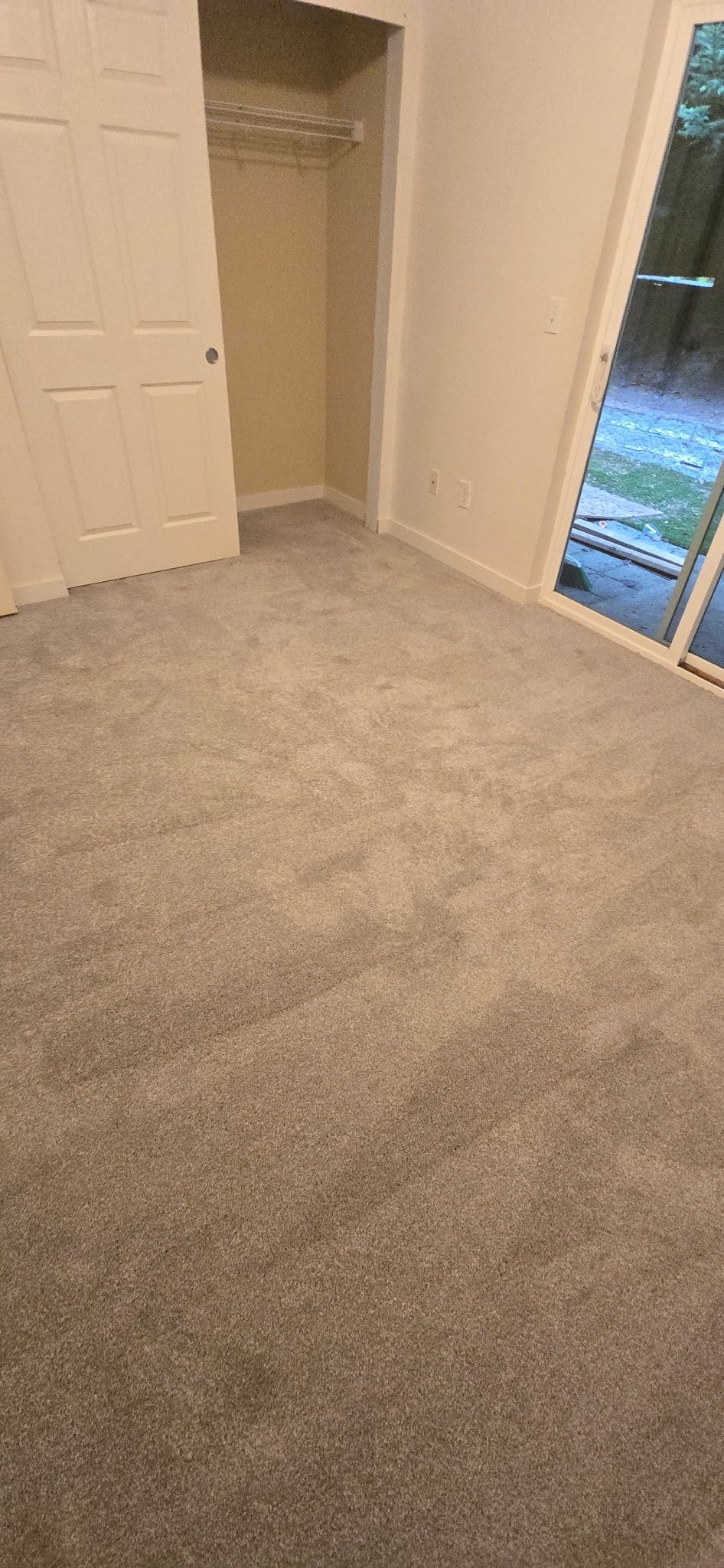 Empty bedroom with gray carpet, a closet, and sliding glass door.