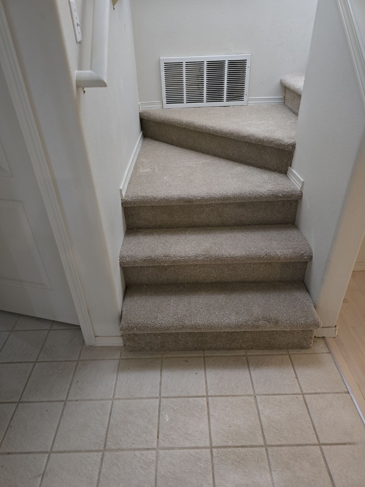 Staircase with carpeted steps, turning to the left, leads upward; floor is tiled.