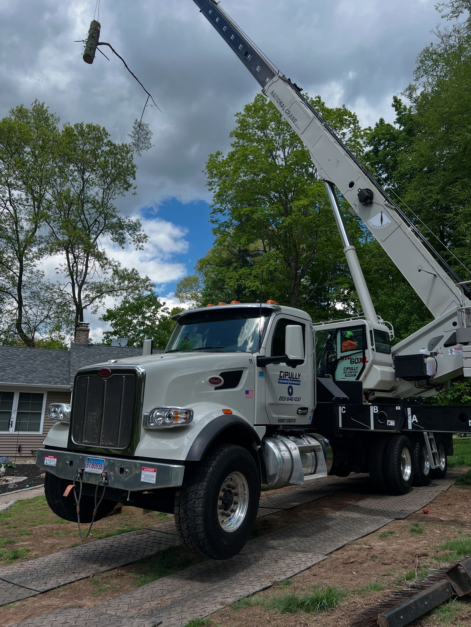 A white truck with a crane attached to it is parked in front of a house.