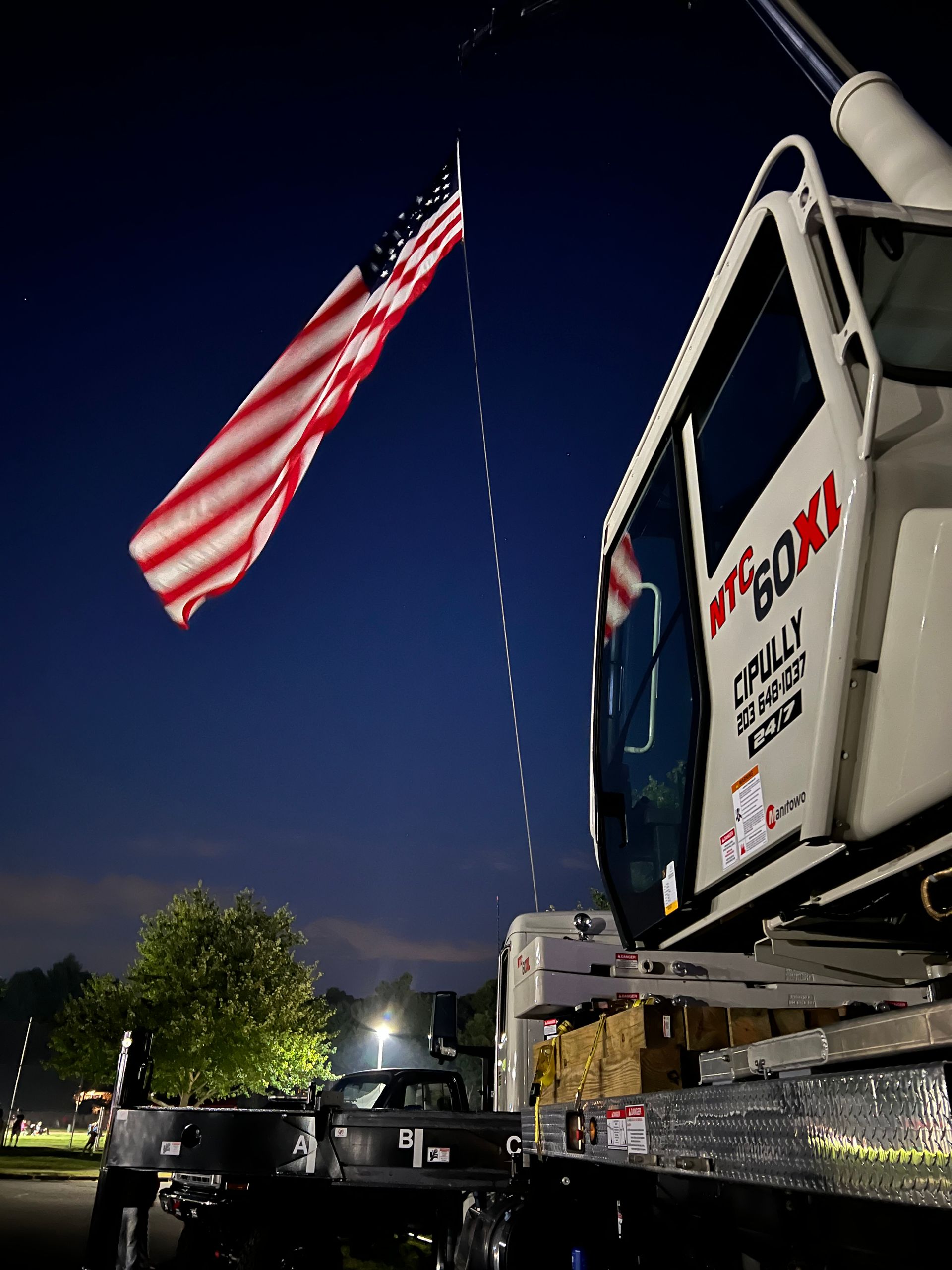 An american flag is flying over a tow truck at night
