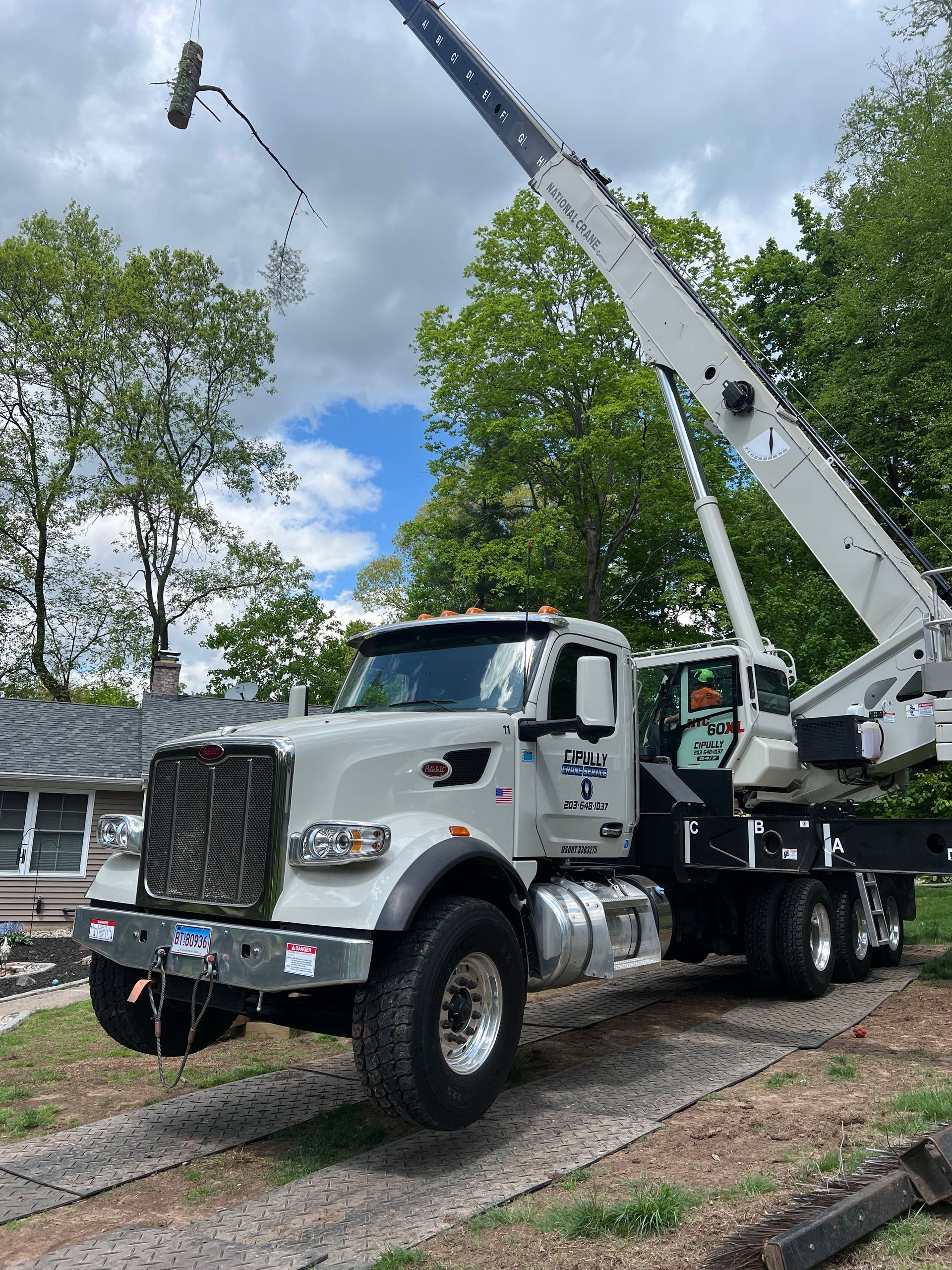 A white truck with a crane attached to it is parked in front of a house.