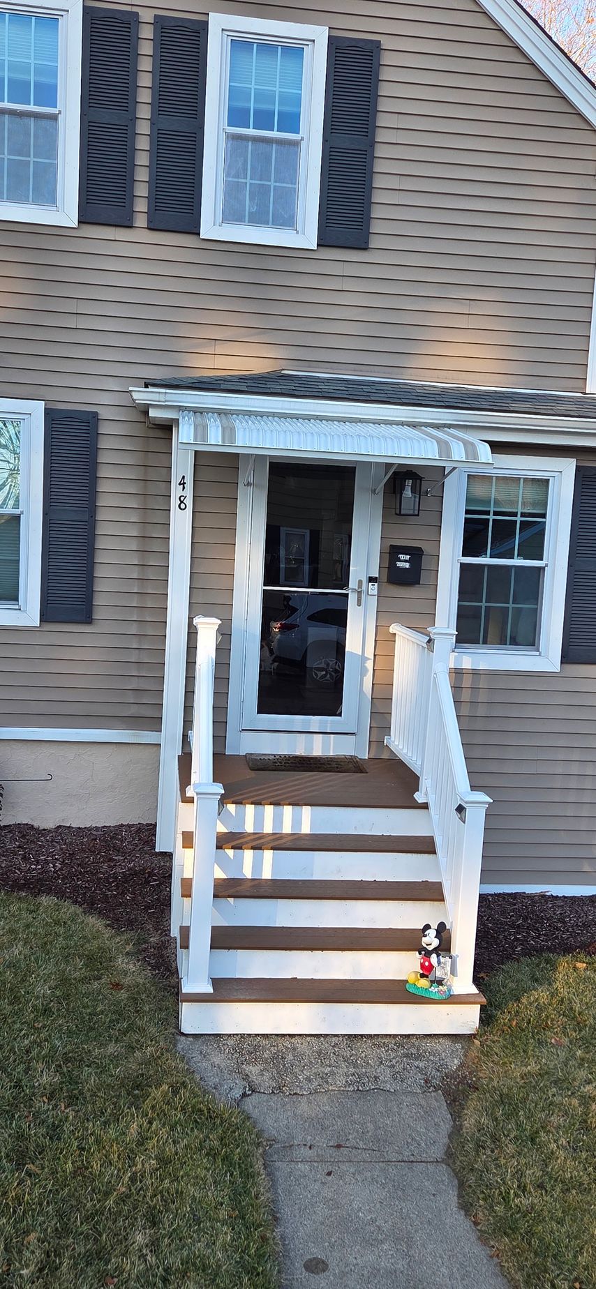 A two-story house with a porch. Brown siding and dark shutters frame the windows. Steps lead to a door.