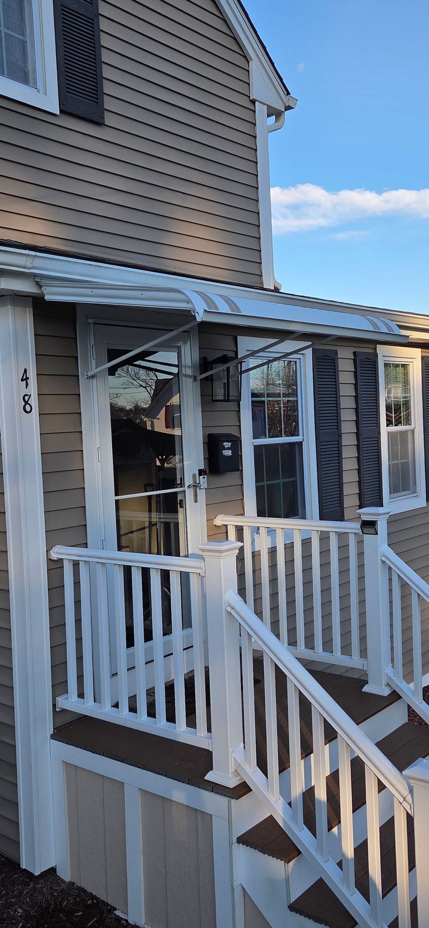 House exterior with porch, steps, and door with window. Tan siding and blue sky.