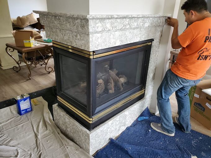 A man in an orange shirt is working on a fireplace.