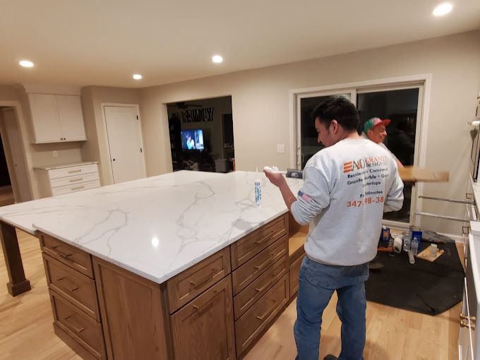 A man is standing in a kitchen painting a counter top.
