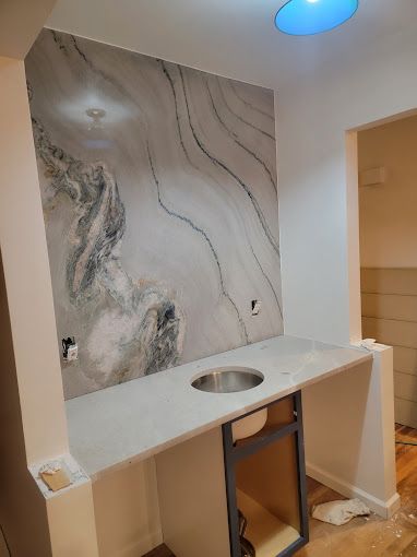 A kitchen with a sink and a marble wall behind it.