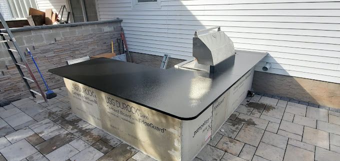 A black counter top is sitting on a patio next to a house.