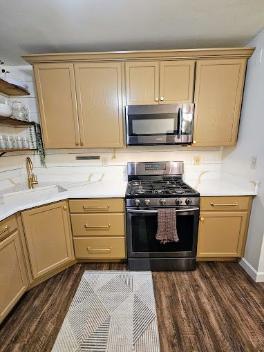 A kitchen with a stove, microwave, sink and cabinets.