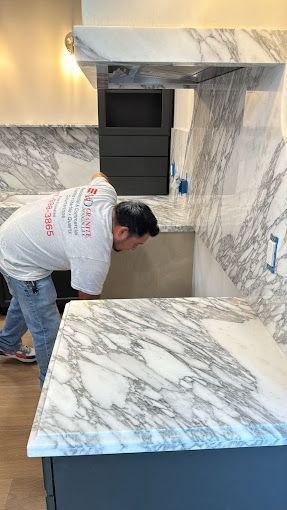 A man is working on a marble counter top in a kitchen.