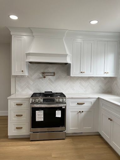 A kitchen with white cabinets, a stove, and a hood.