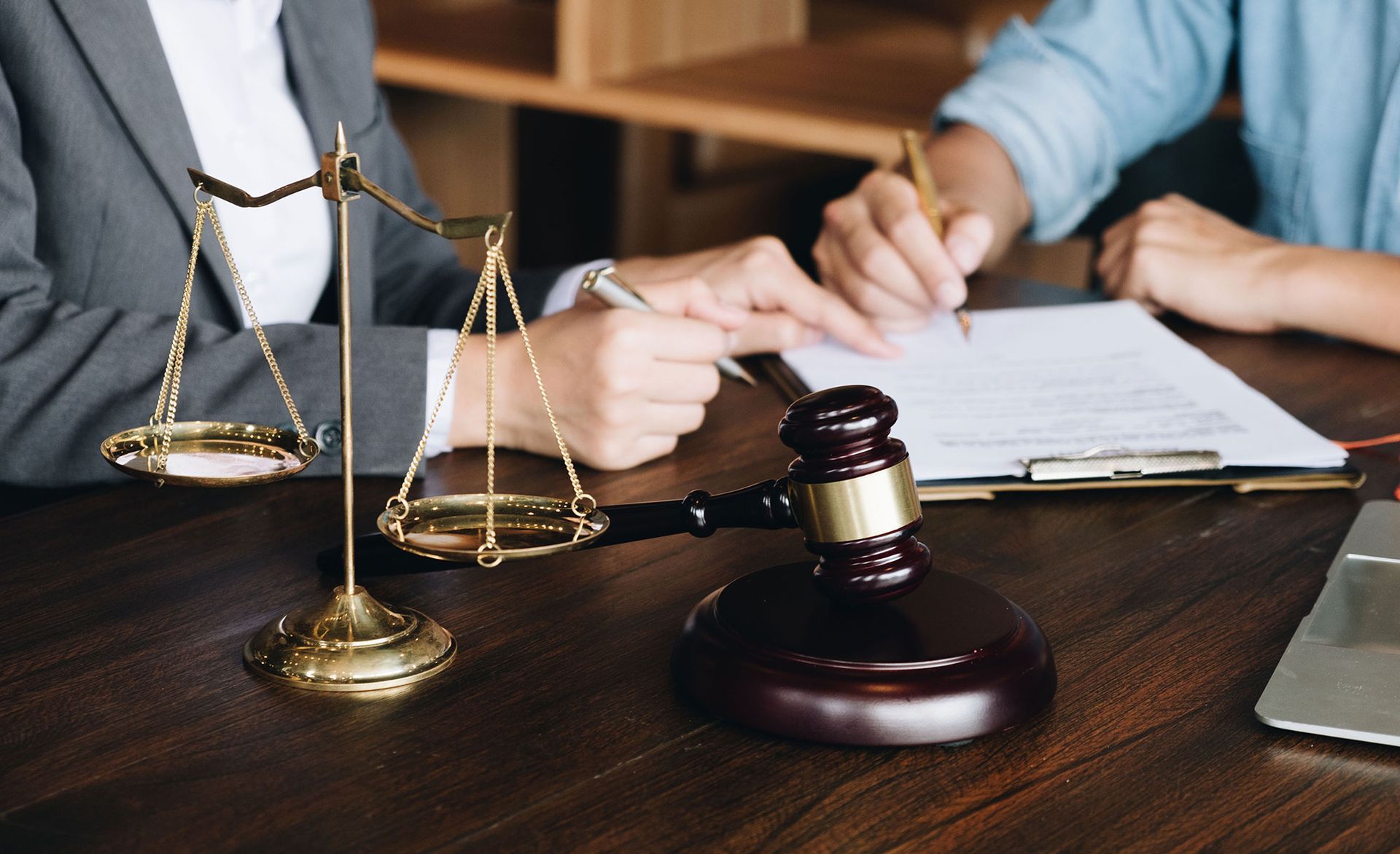 Scales of justice, gavel, and two people signing documents at a desk.