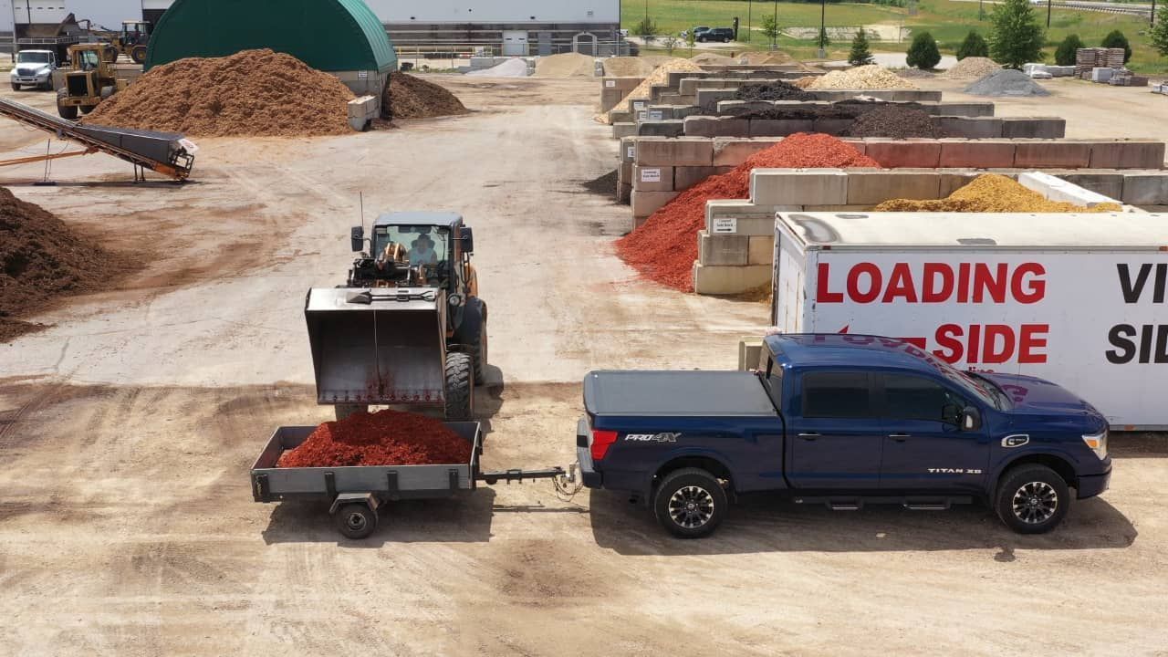 A blue truck is towing a trailer with a loading side sign in the background.