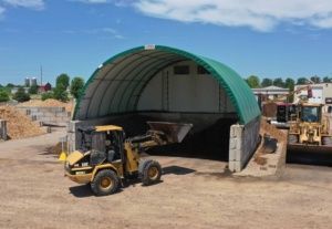 A yellow tractor is parked in front of a green dome.