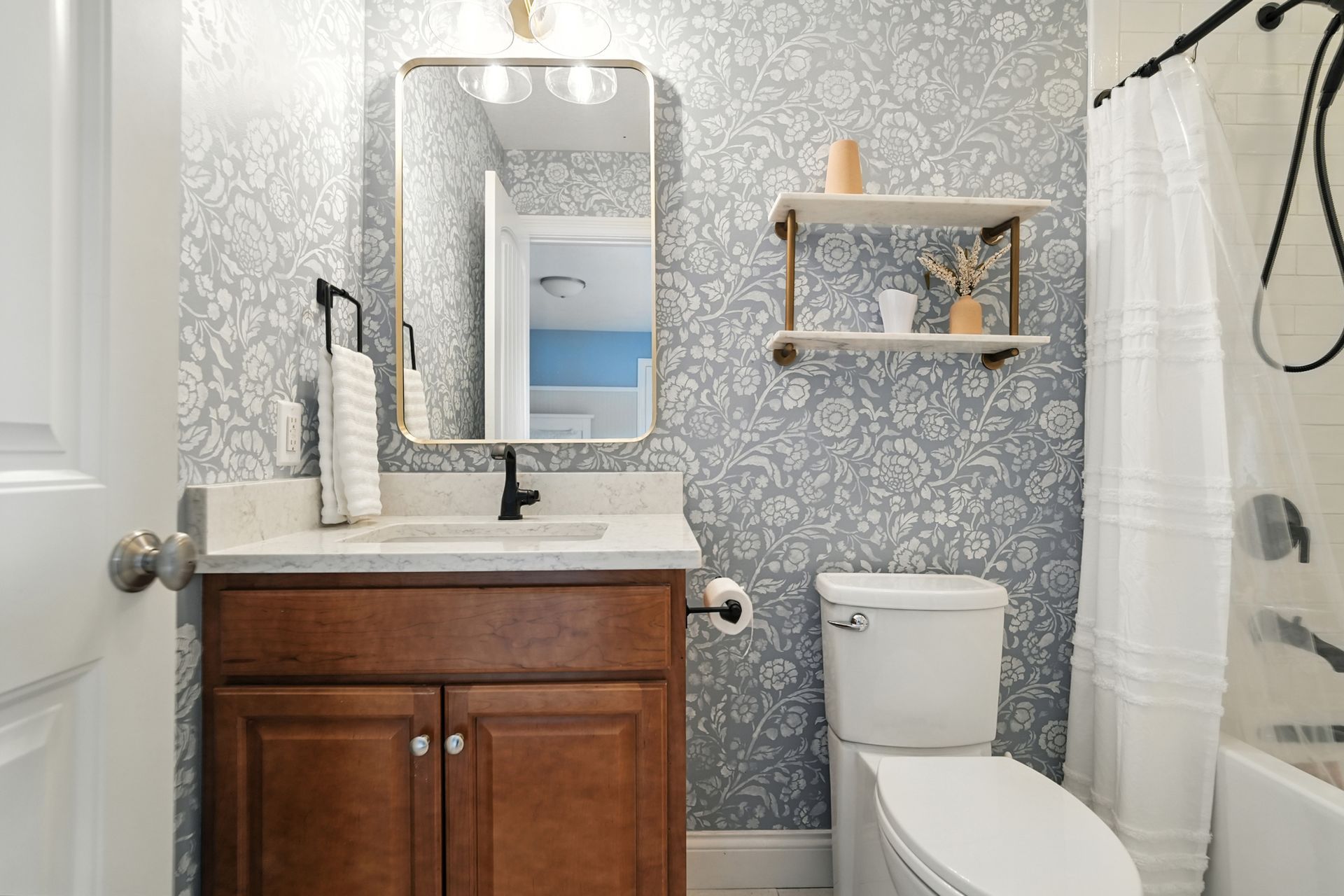 Bathroom with floral wallpaper, brown vanity, and a mirror above the sink.