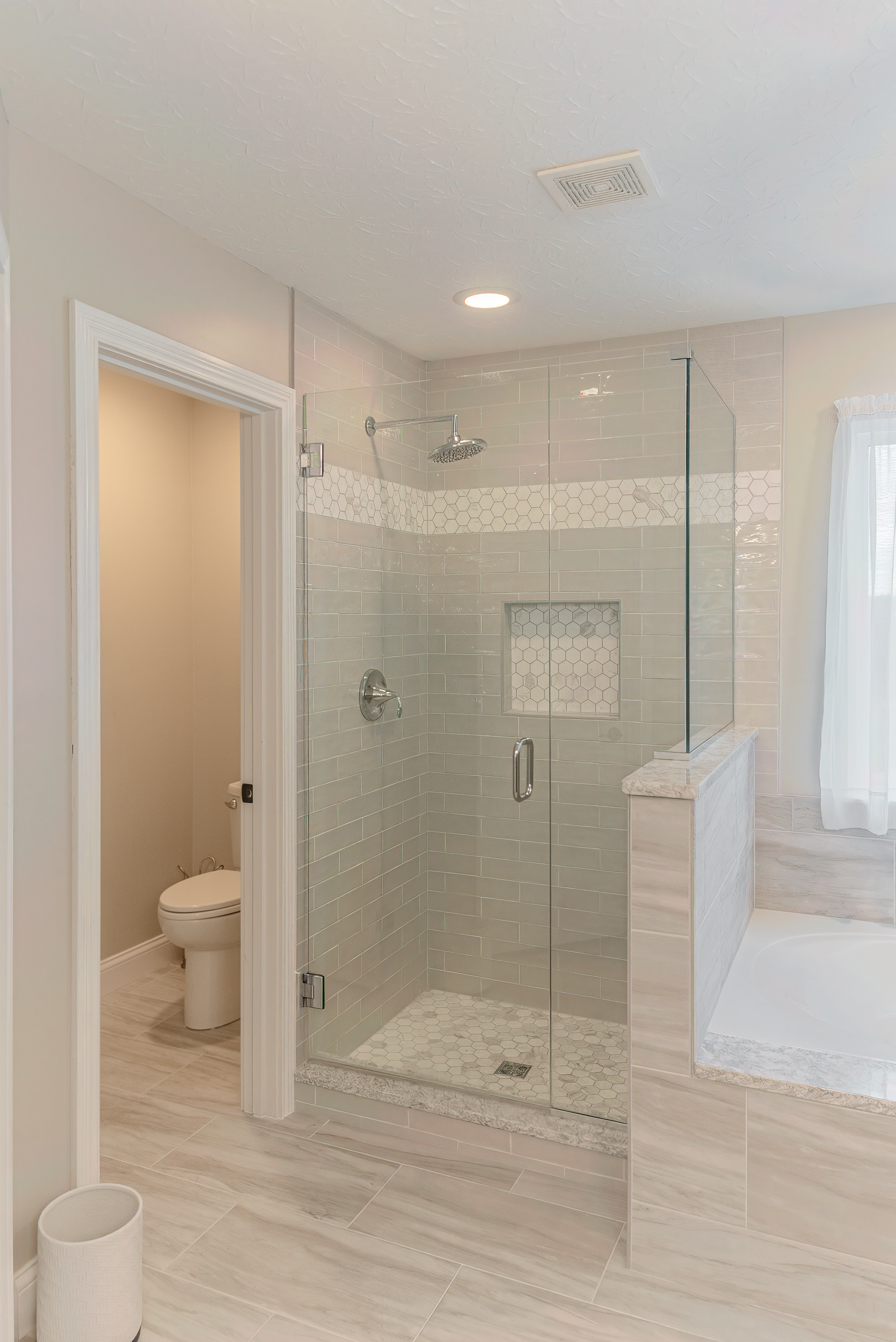 Modern bathroom with glass shower, toilet, and built-in tub. Light-colored tile and walls.