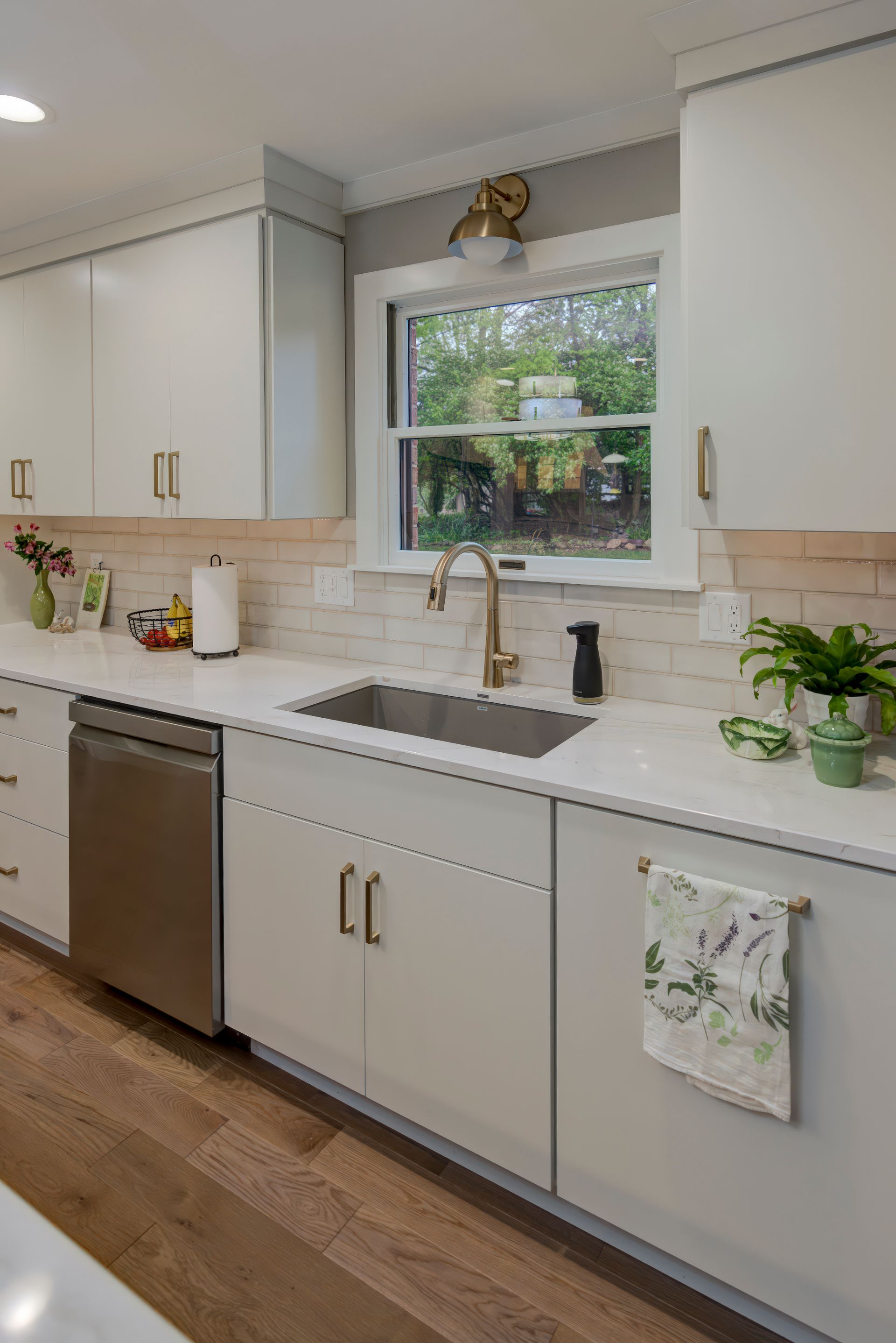 A kitchen with white cabinets, a sink, a dishwasher, and a window.