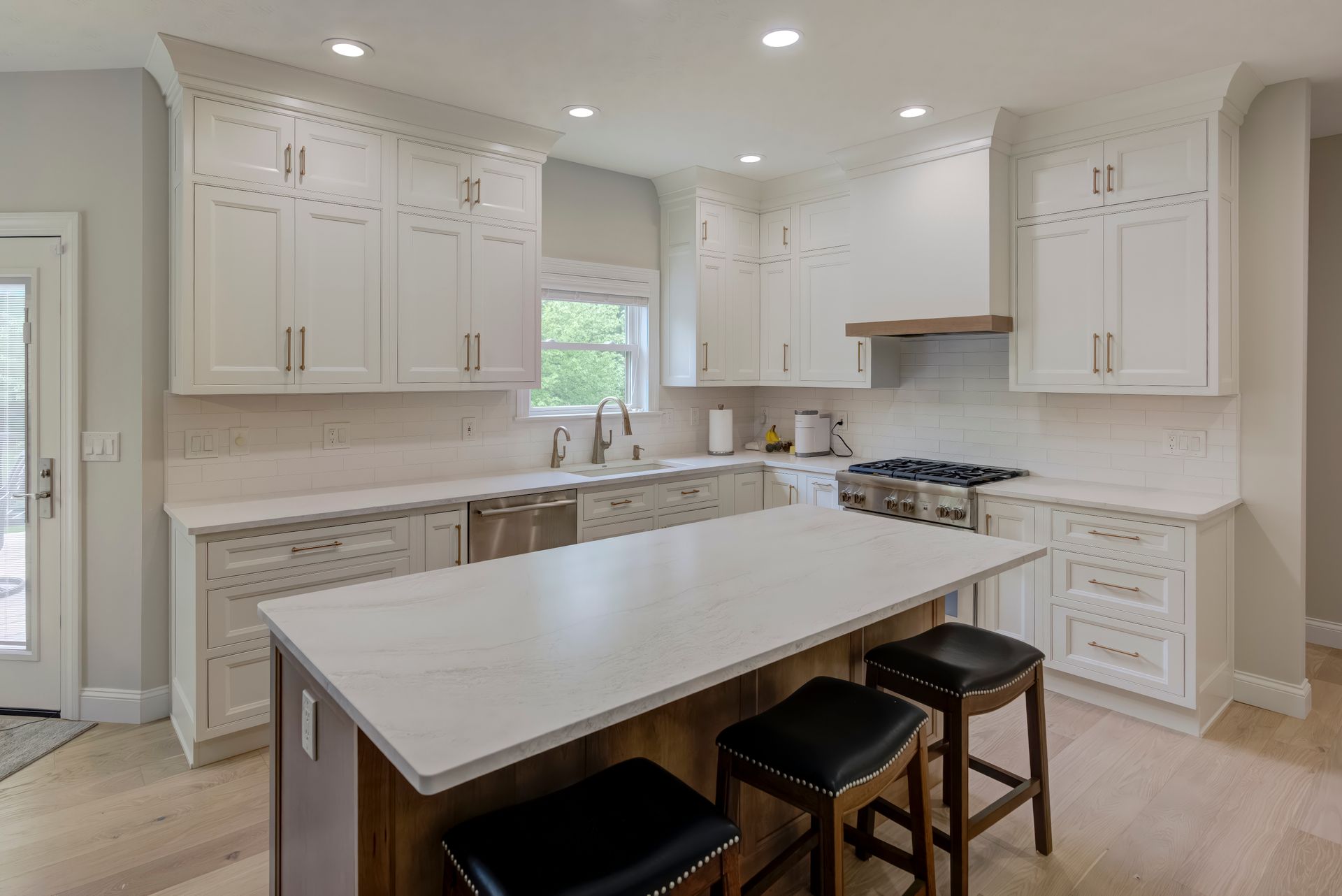 A kitchen with white cabinets, a large island, stools and a stove.