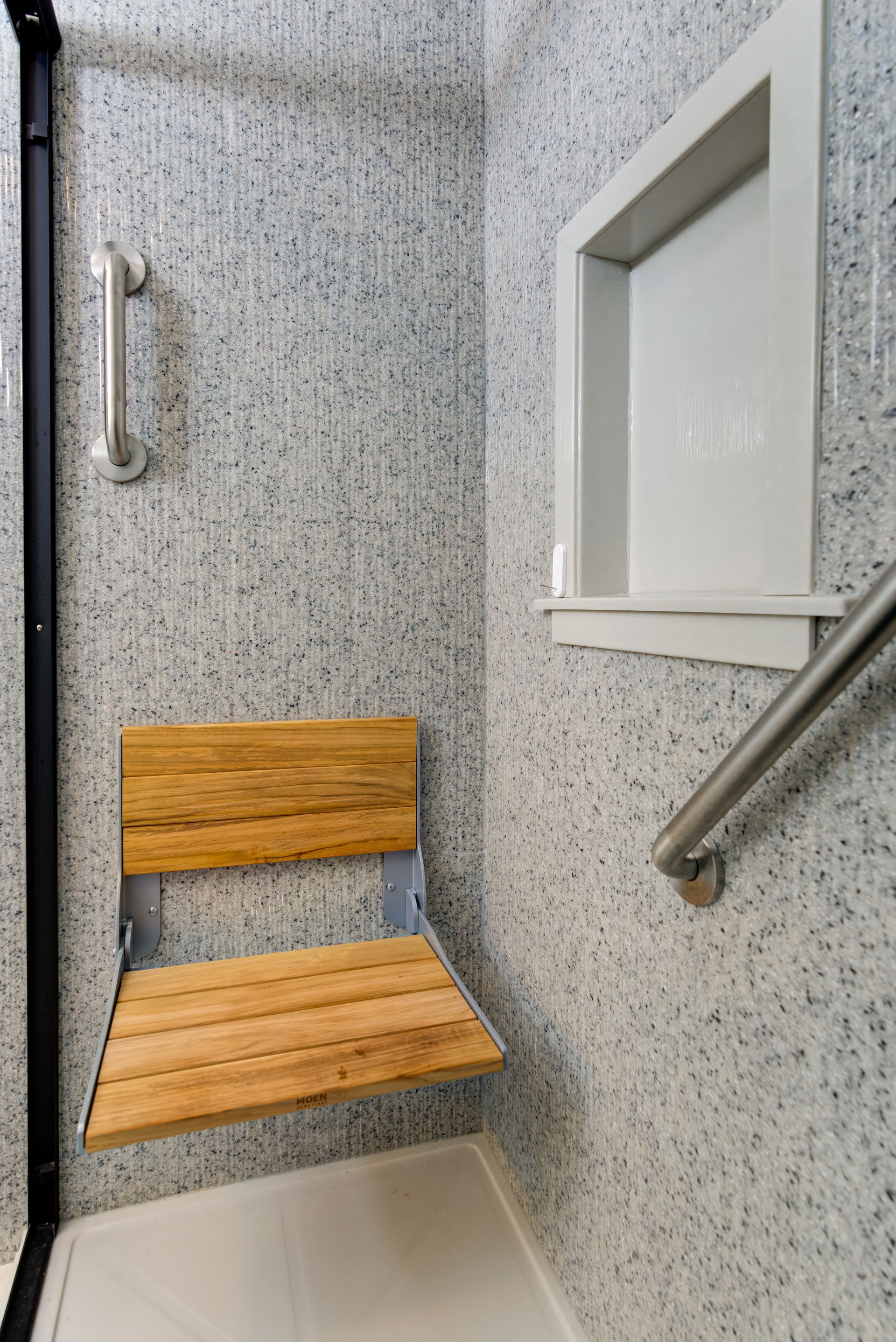 A bathroom with a wooden seat and a stainless steel railing.