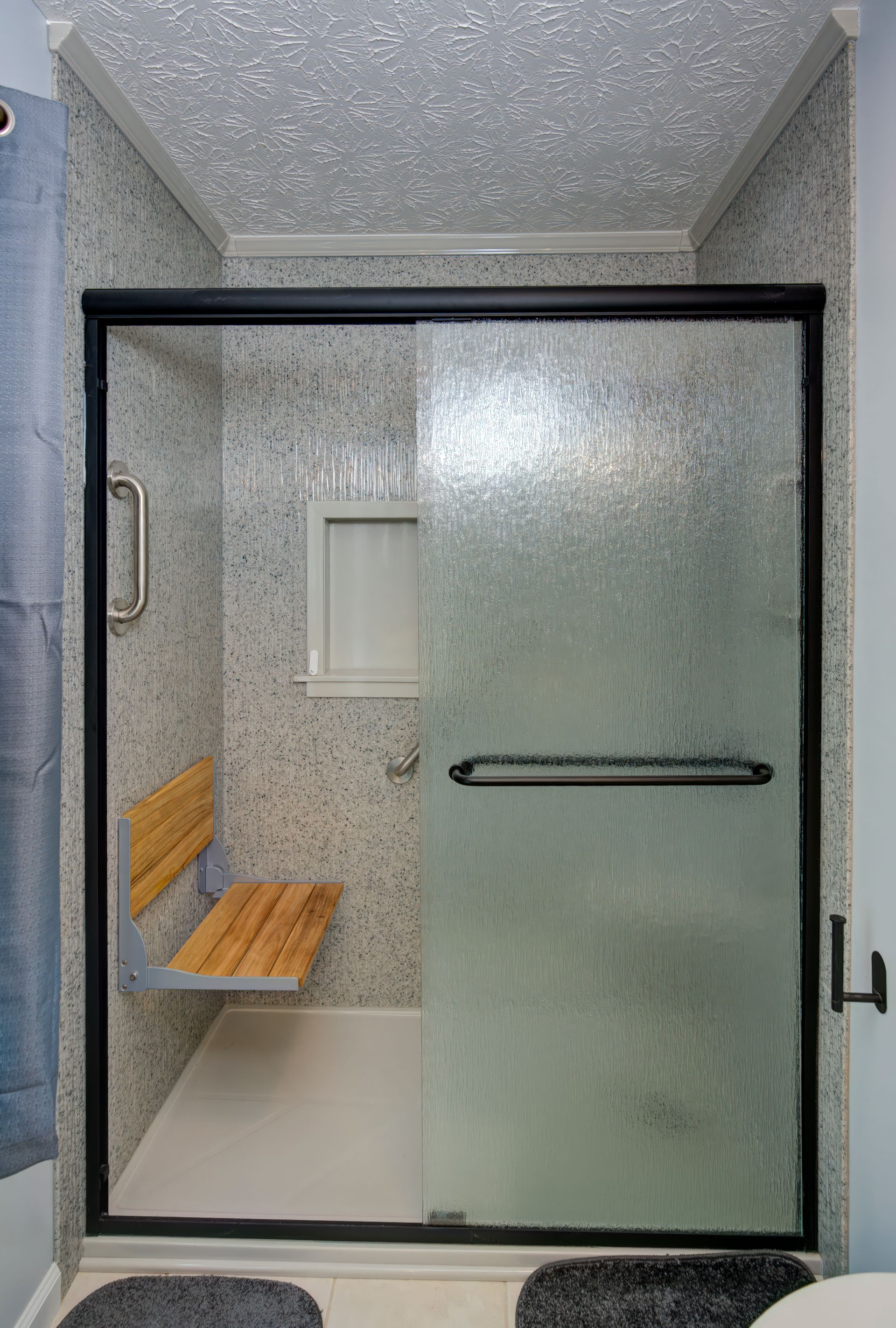 A bathroom with a sliding glass shower door and a wooden bench.