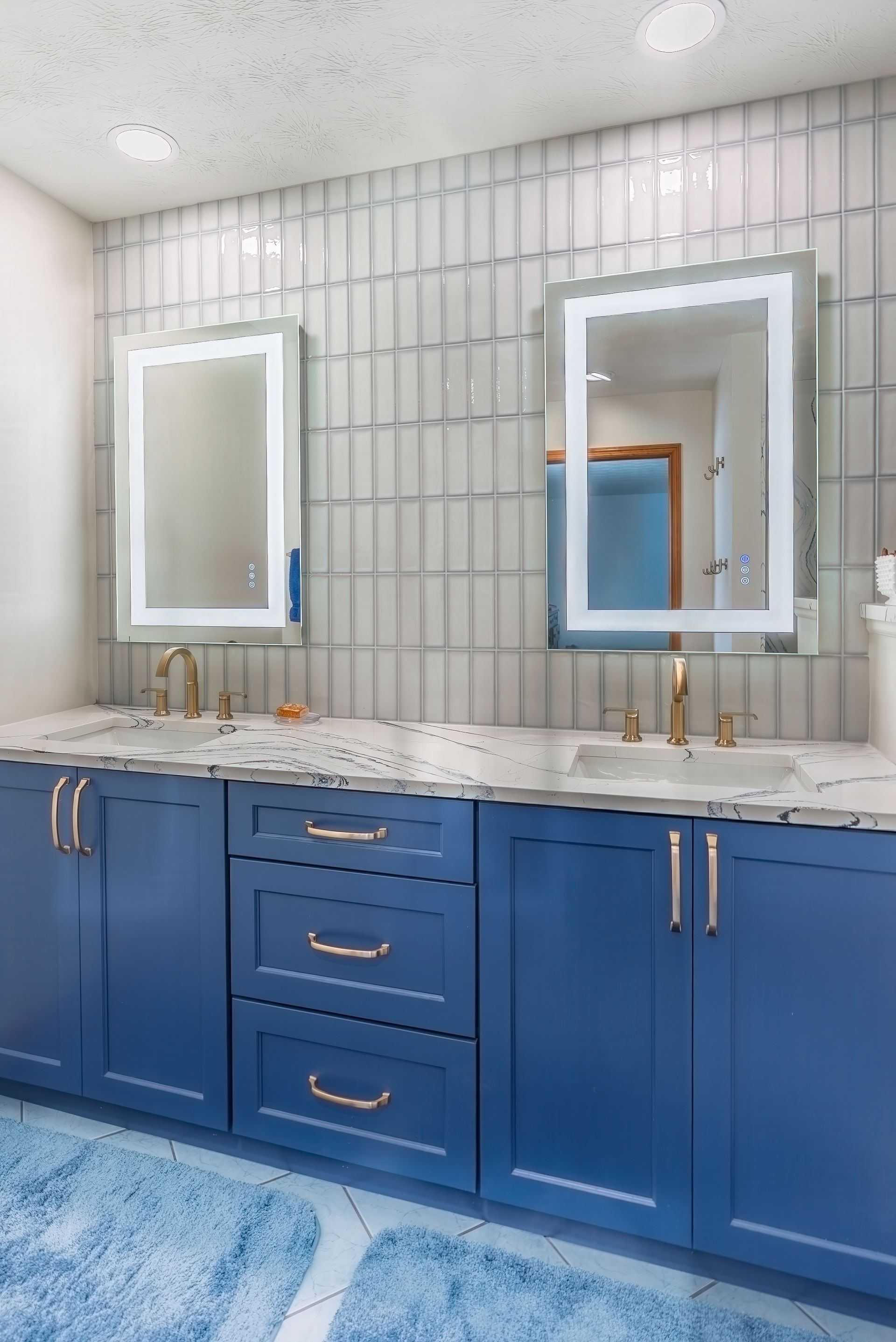 A bathroom with blue cabinets, two sinks, two mirrors and a blue rug.