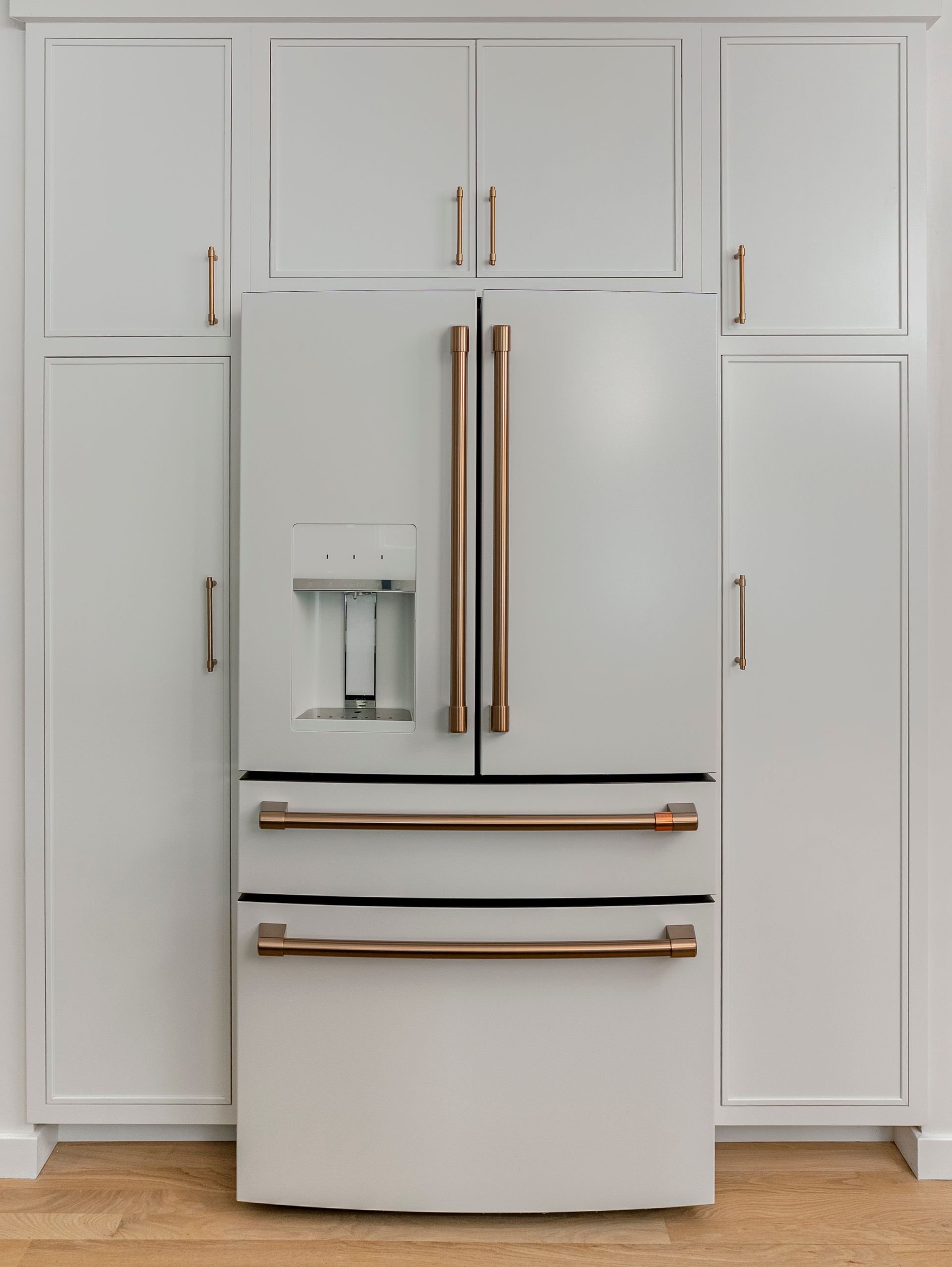 A white refrigerator with copper handles is sitting in a kitchen.