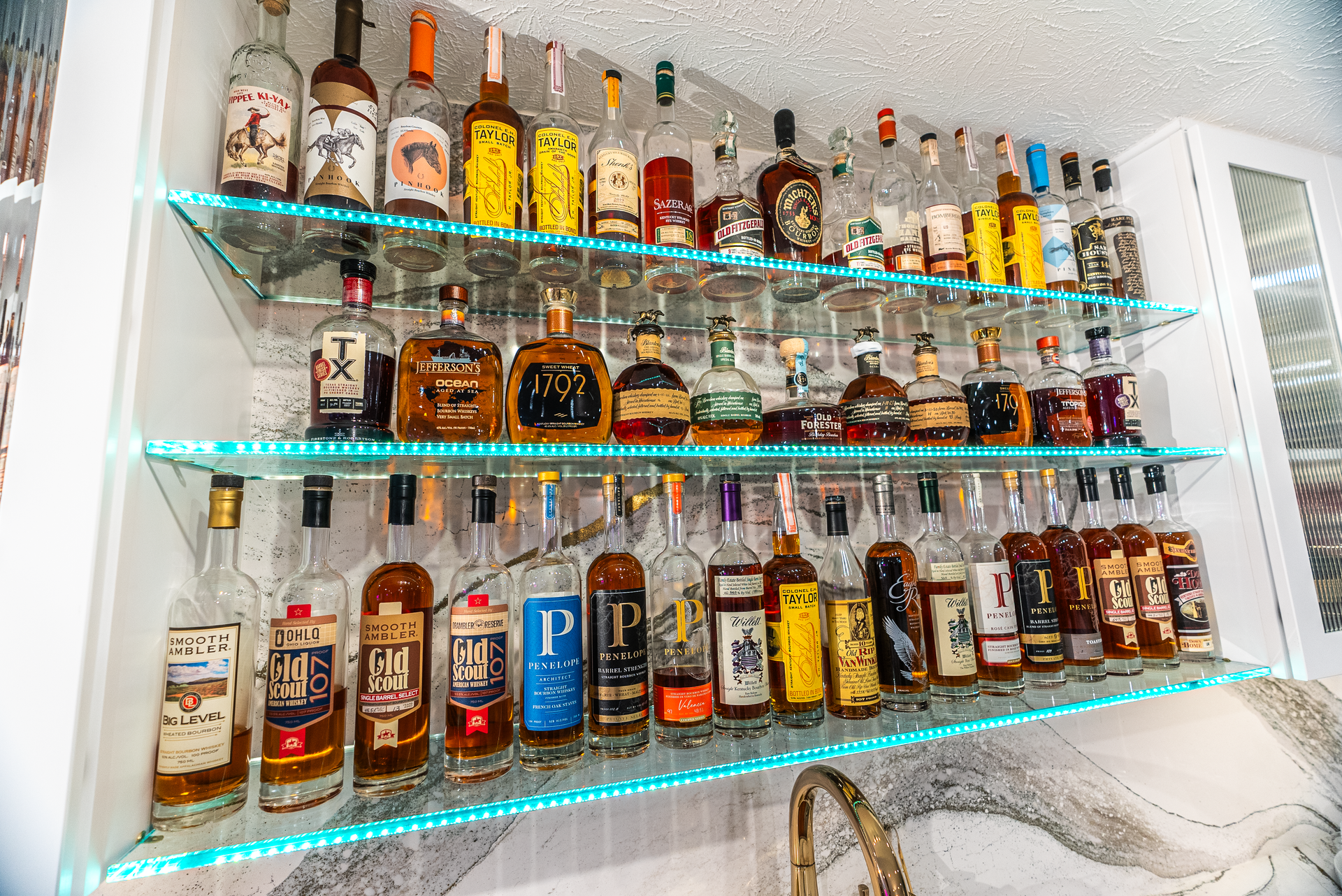 Liquor bottles on lit glass shelves in a home bar.